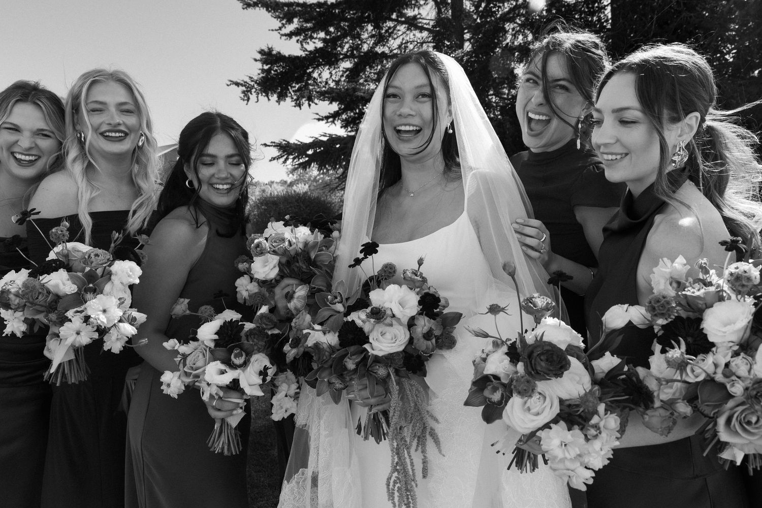 Wedding party group photo with bridesmaids in brown dresses holding colorful floral bouquets.
