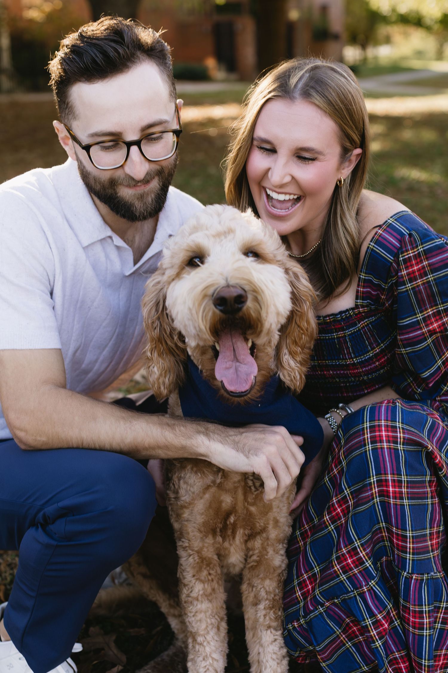 A couple cuddles with their happy goldendoodle during an outdoor autumn photography session.