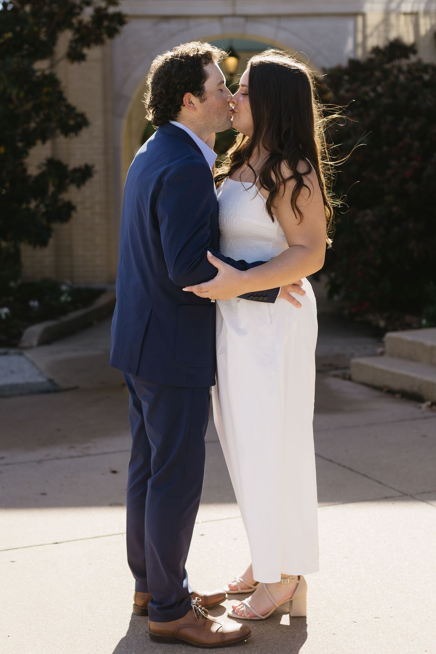 A couple in navy suit and white dress share an intimate moment outdoors.