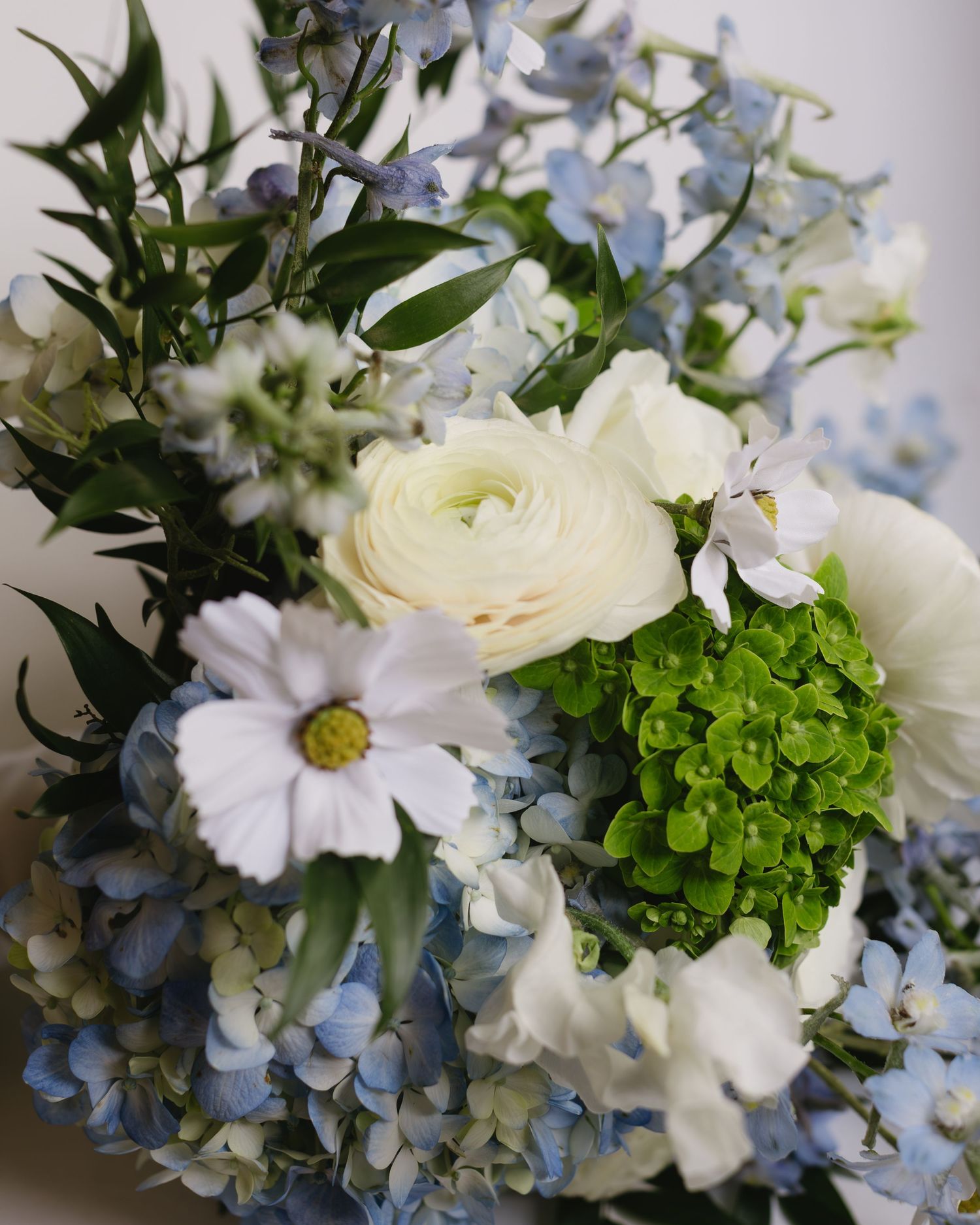Elegant floral arrangement featuring white roses, hydrangeas, and delicate blue flowers with fresh greenery.