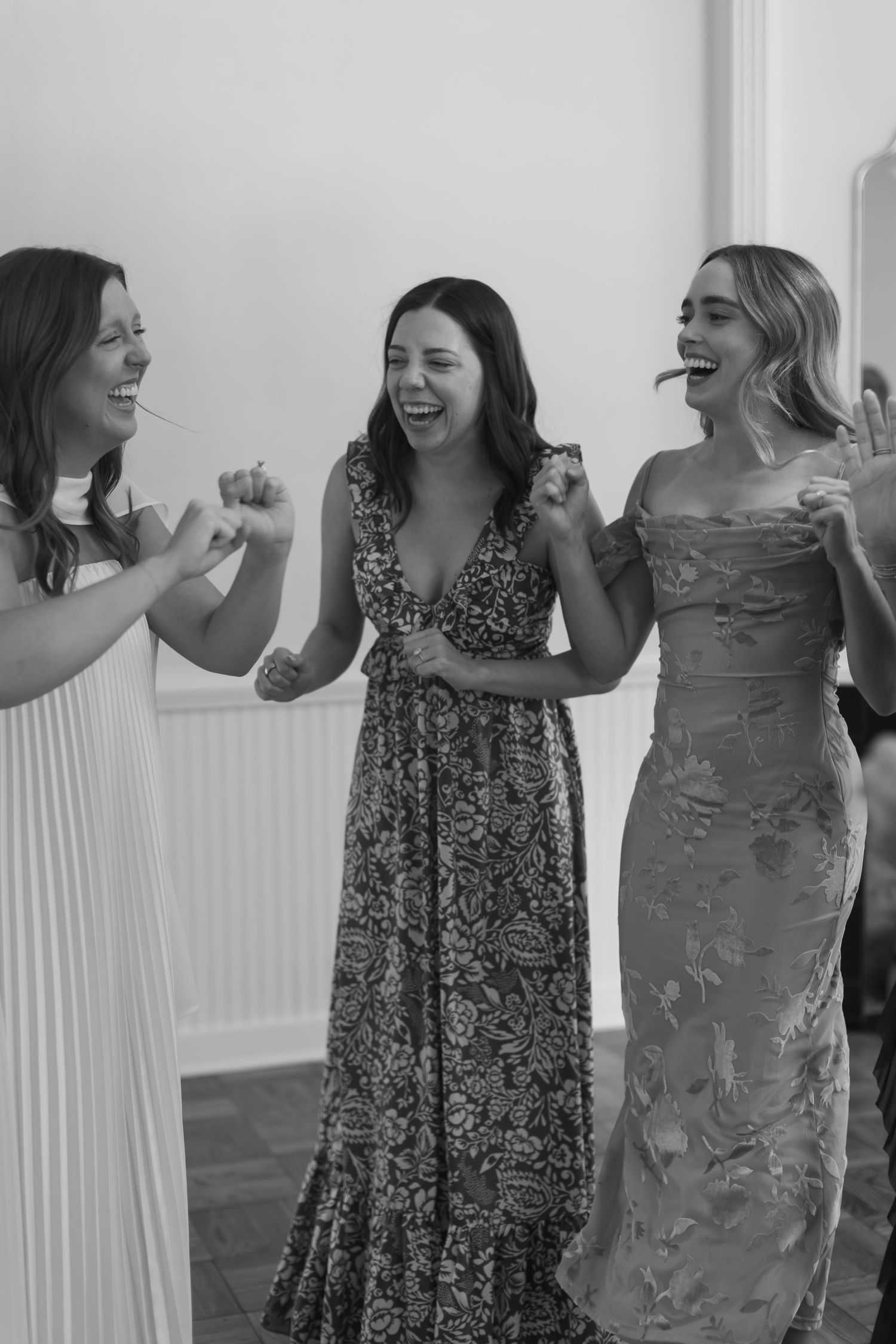 Black and white photo of three women in formal dresses sharing a joyful moment.