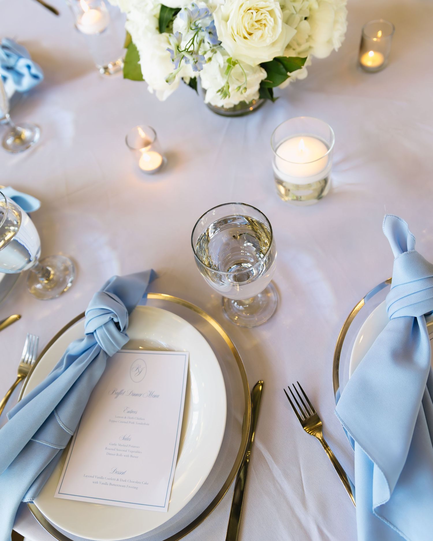 Wedding table decor featuring white flowers, candles, and light blue napkins.