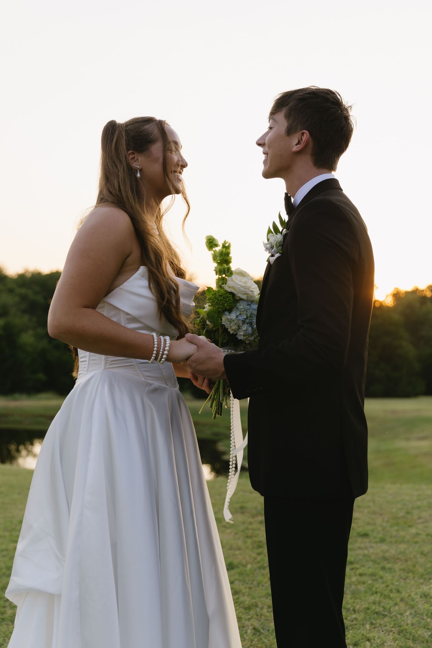 A sunset wedding portrait showing the couple in formal attire on a grassy field.