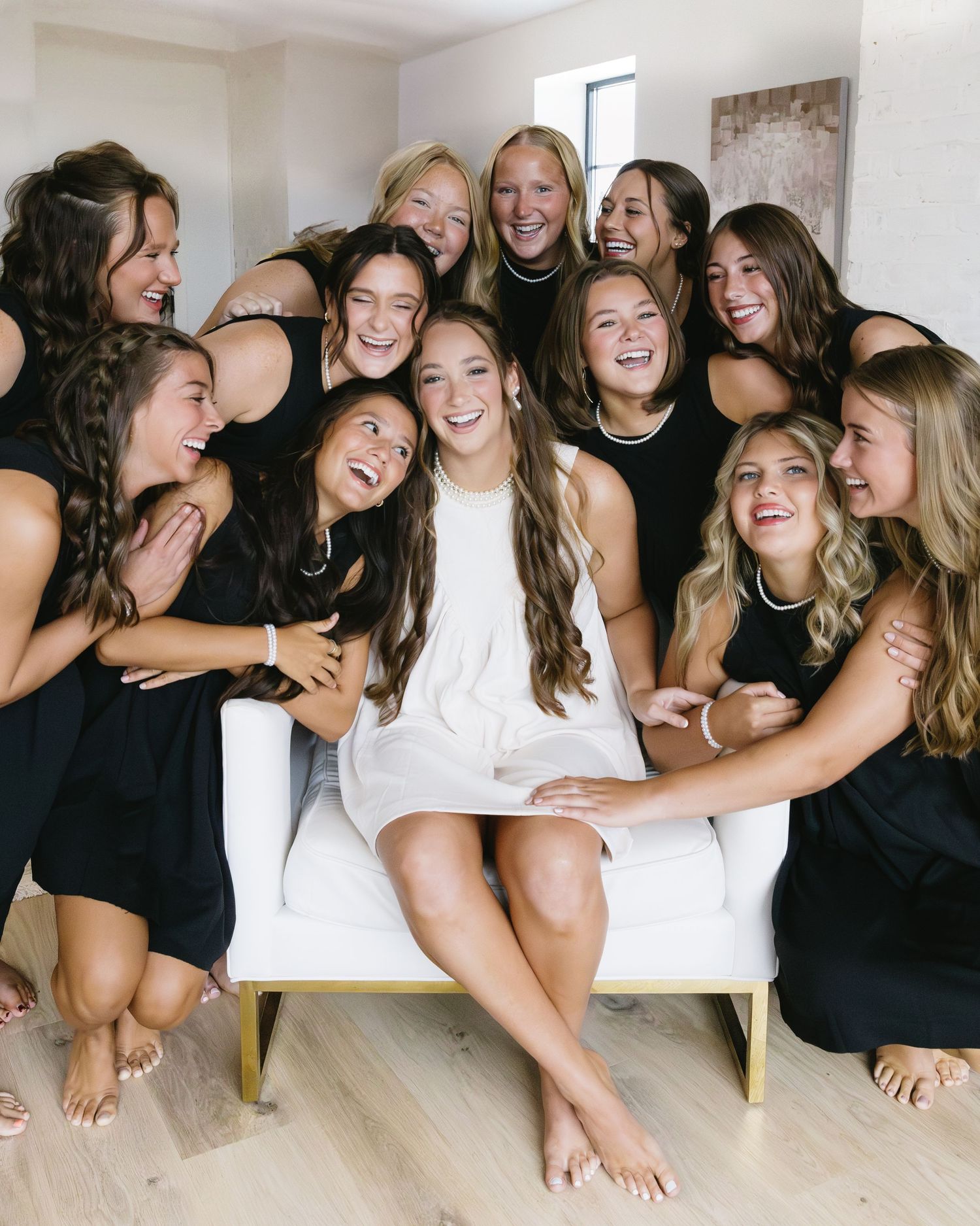 Group photo of bridesmaids in black and white dresses laughing together in a bright room.