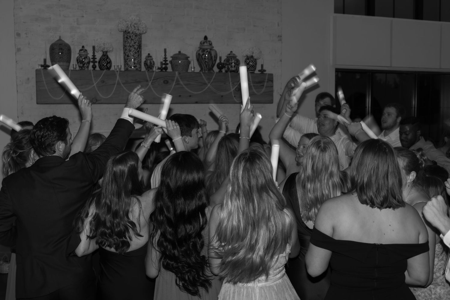 Dark silhouettes of wedding guests dancing with hands raised on dance floor.