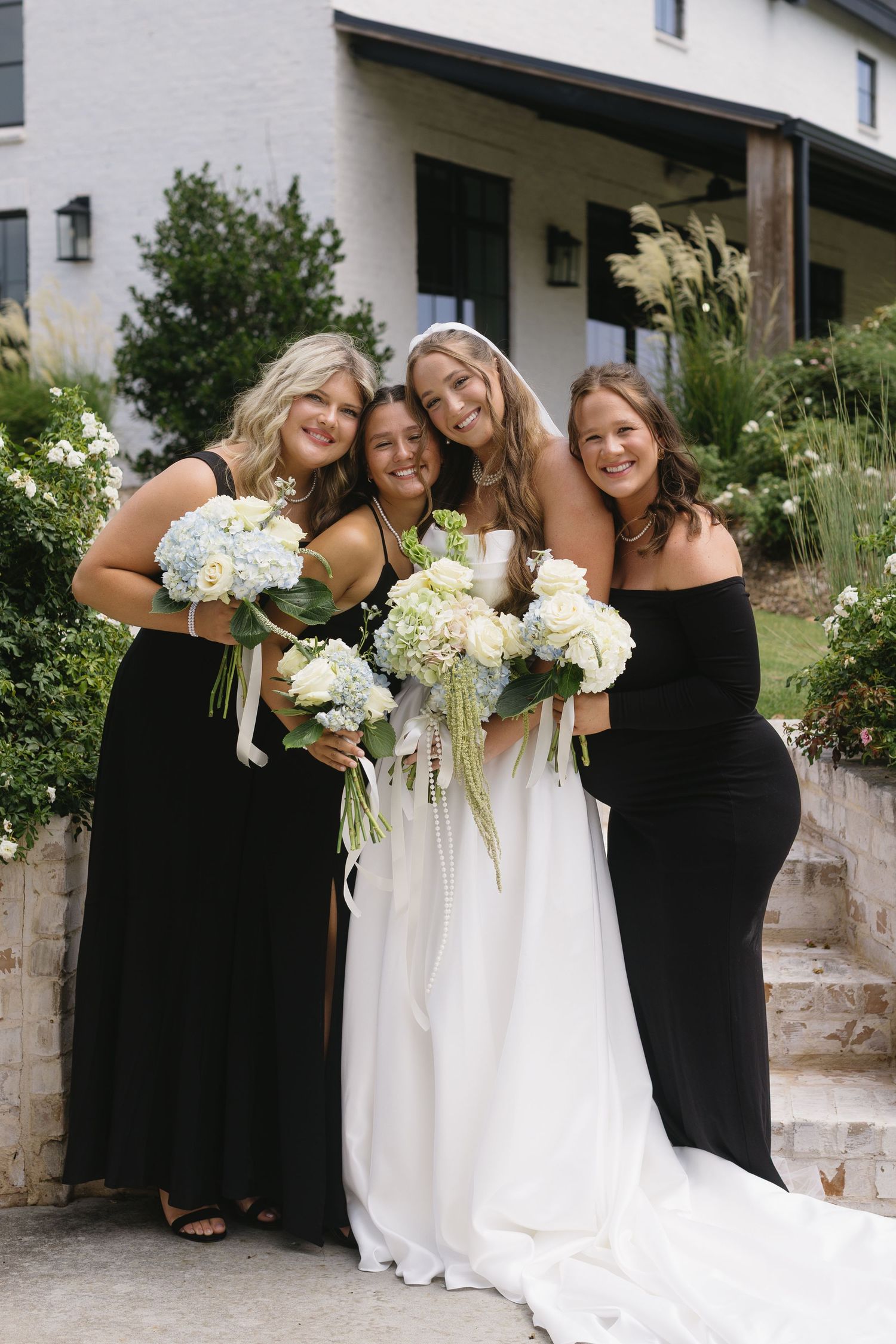 Wedding party photos with bridesmaids in black dresses holding white bouquets alongside the bride.