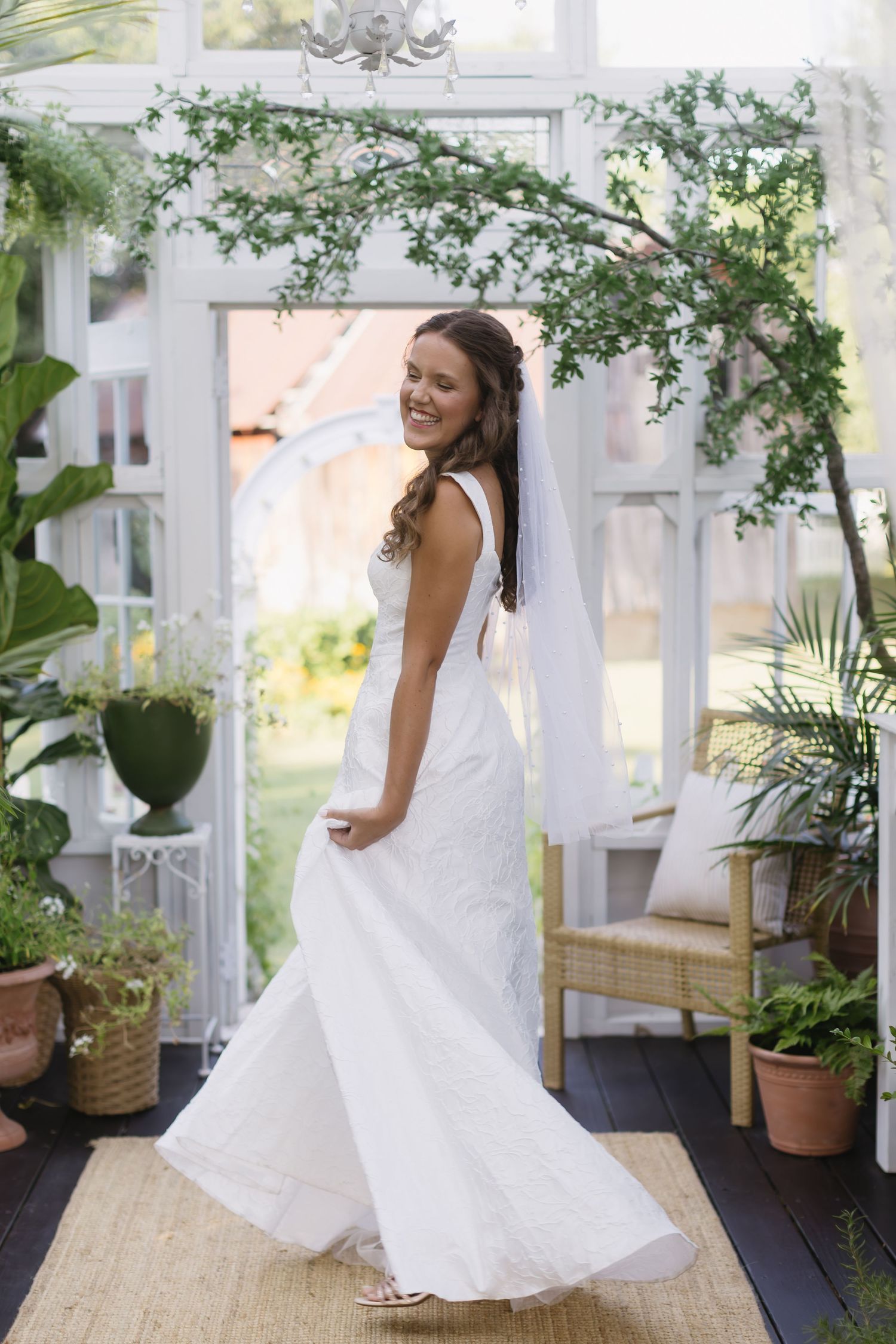 A flowing white wedding dress is showcased in an elegant greenhouse setting with climbing vines and greenery.
