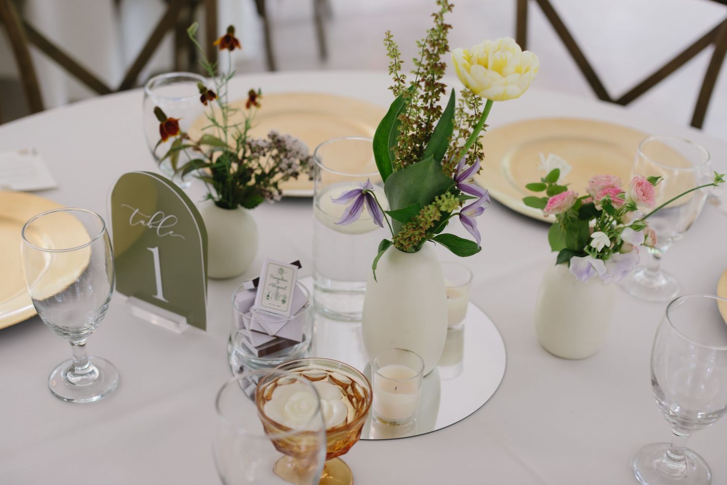 Delicate floral centerpieces and place settings on white linen tablecloths with soft natural lighting.