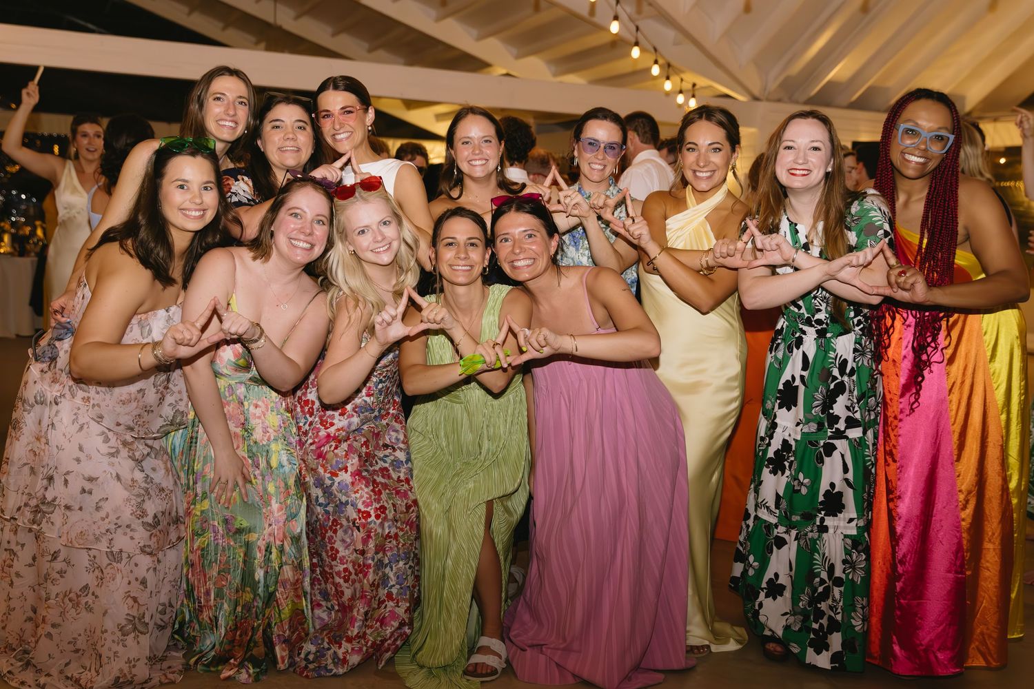 Wedding guests in colorful dresses enjoying the reception under draped ceiling with string lights.