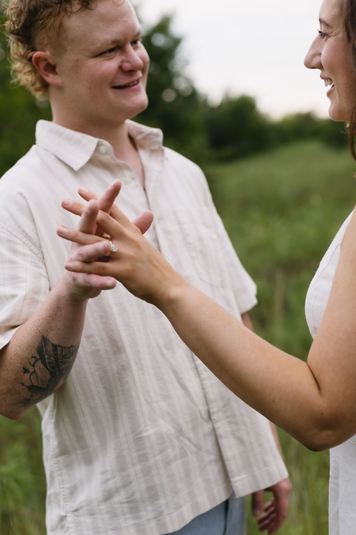 A couple in white clothing share a playful moment in a sunlit meadow.