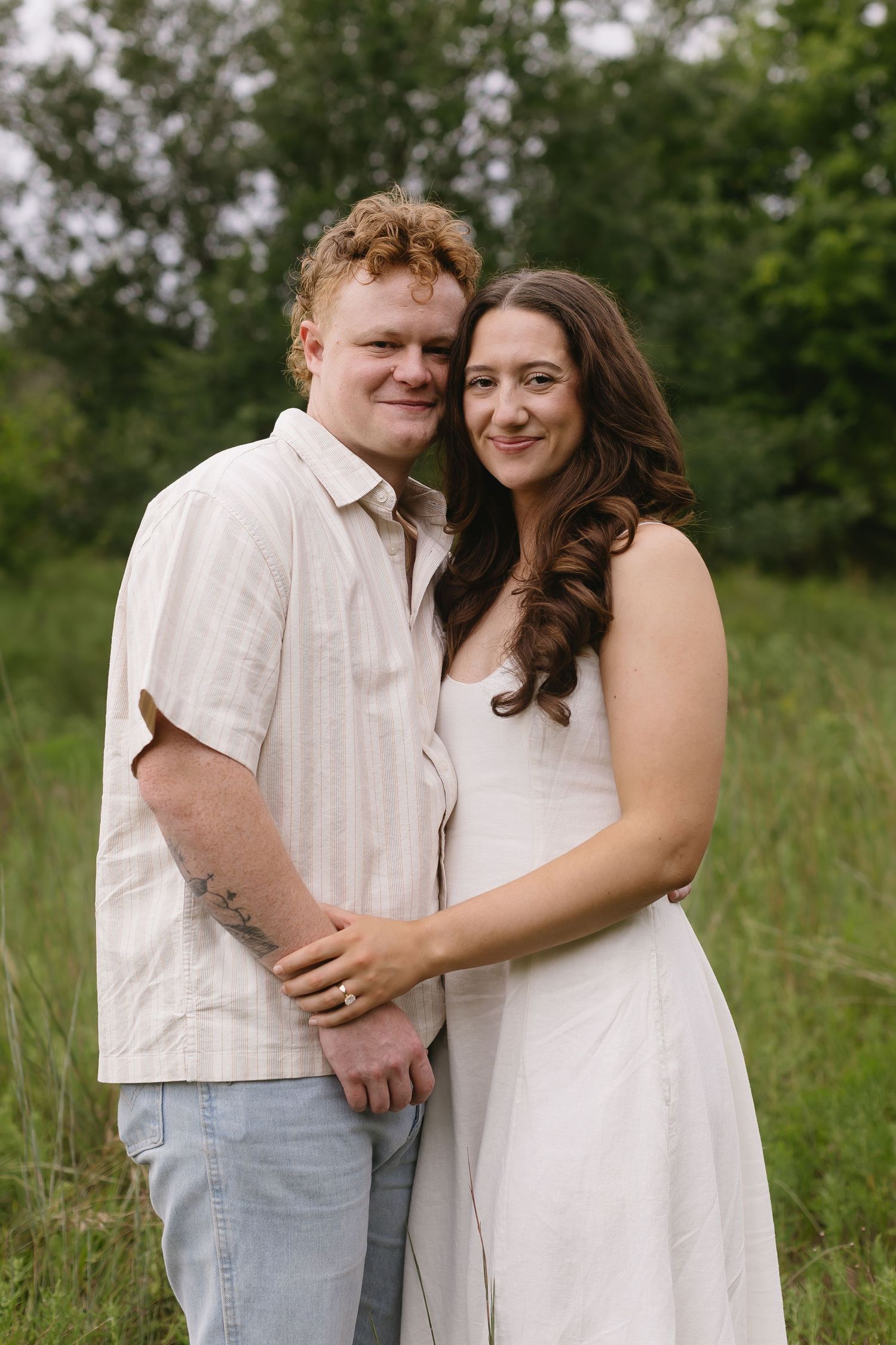 Two people in white clothing share tender moments outdoors in a grassy field.