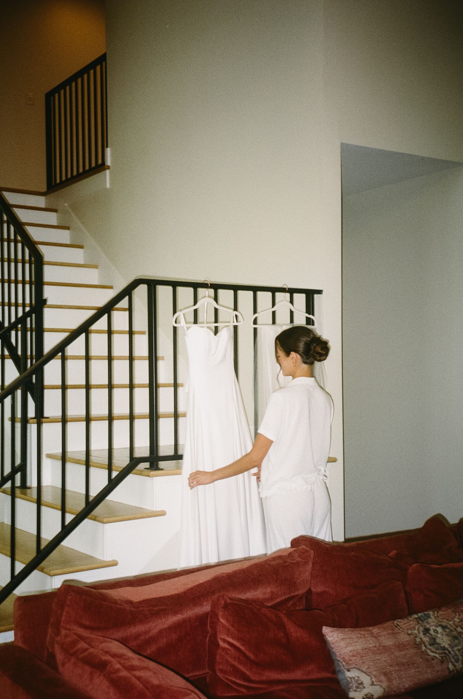 A white wedding dress hanging on a staircase railing in a home.