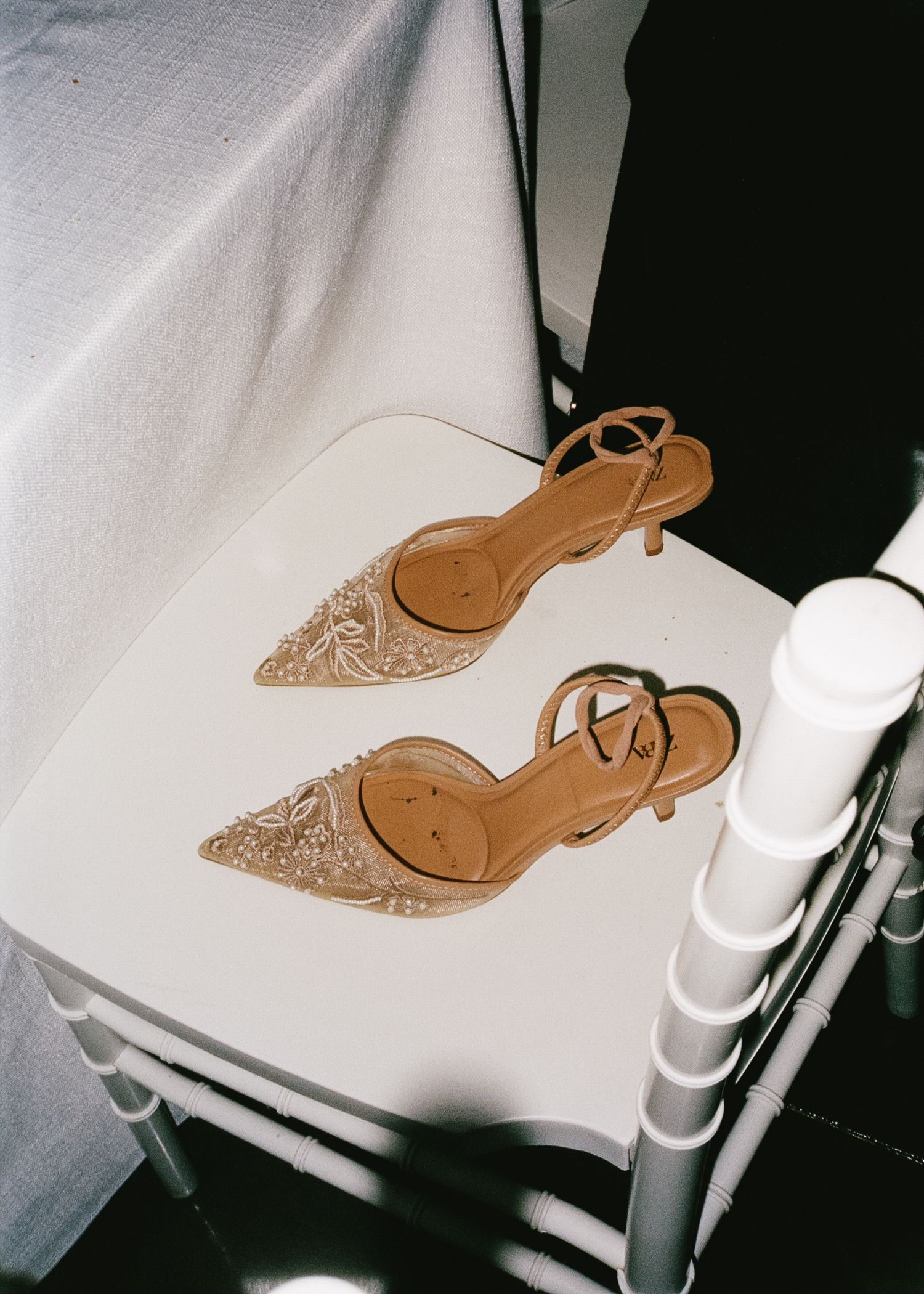 Beige glittery kitten heel slingback shoes placed on white chair at wedding venue.