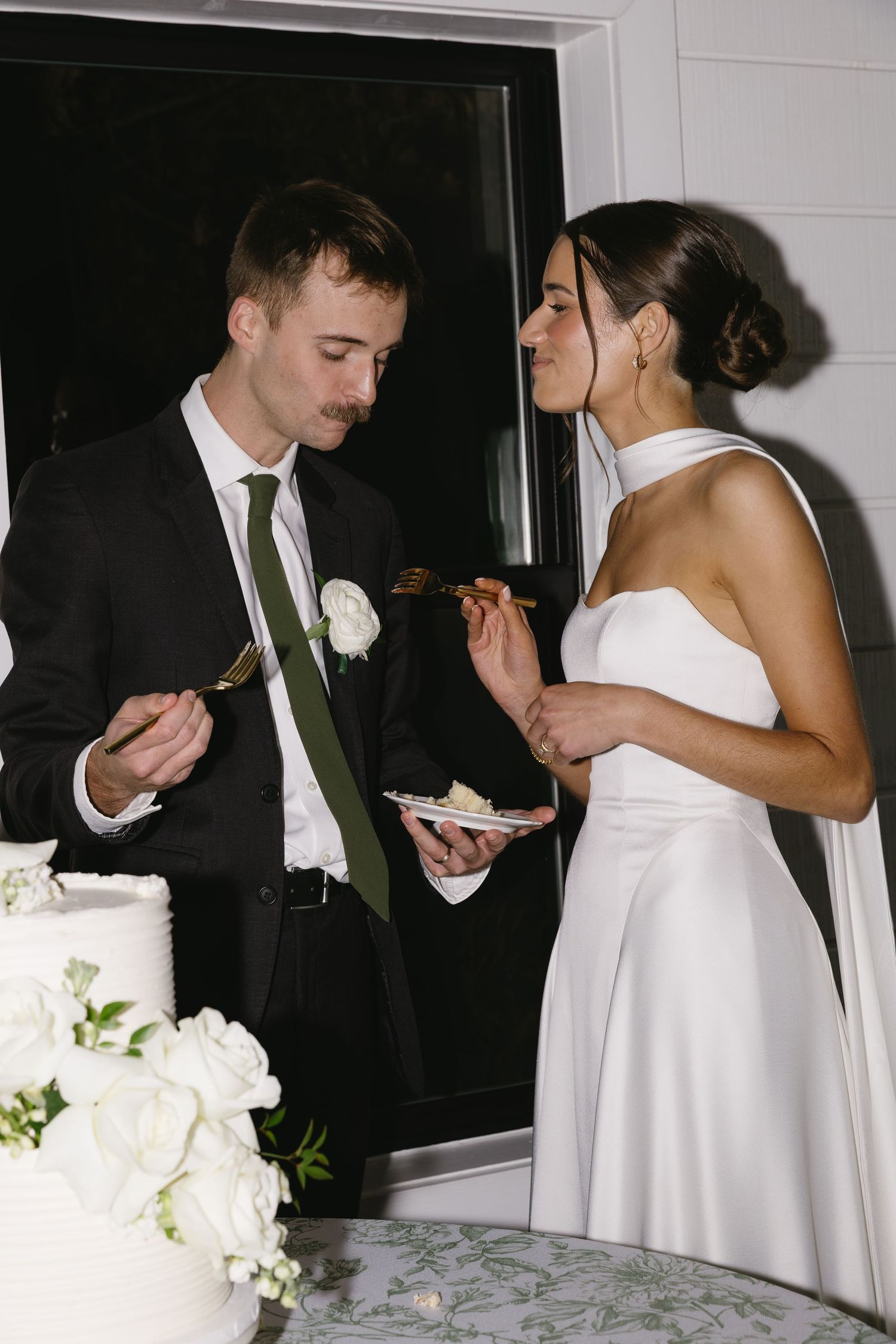 Wedding couple sharing cake at their reception in front of white floral arrangements.