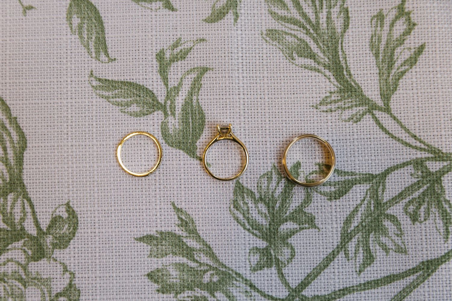 Wedding rings displayed on a floral patterned fabric with delicate green leaf designs.
