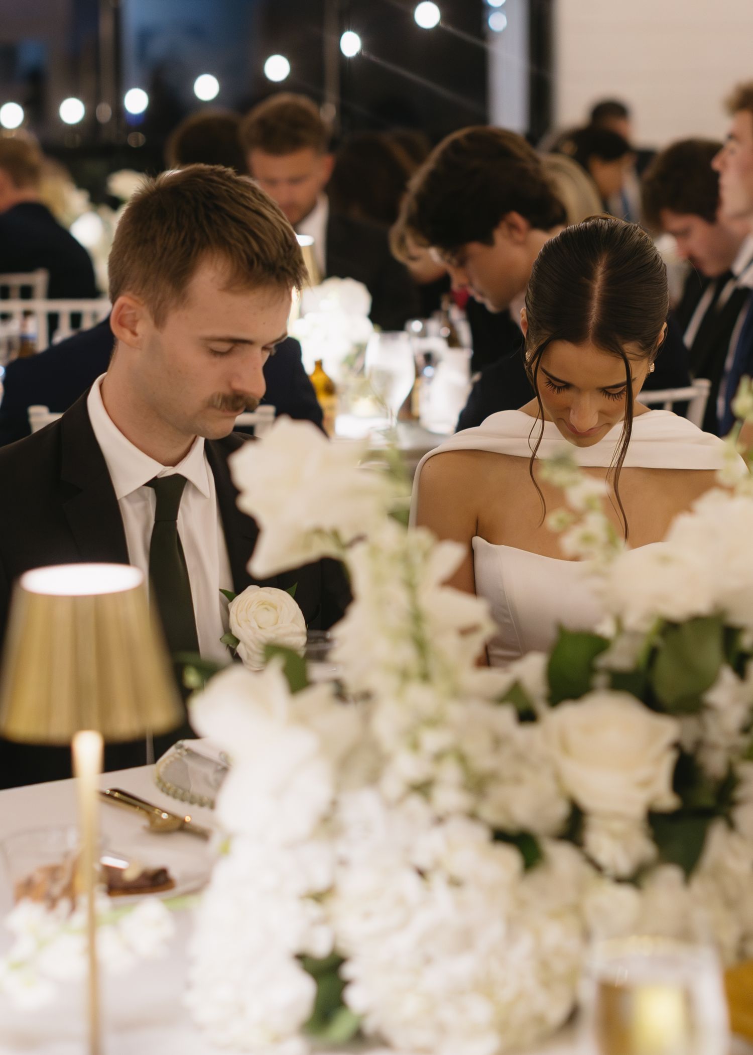 Intimate wedding reception dinner with white floral centerpieces and soft candlelight.