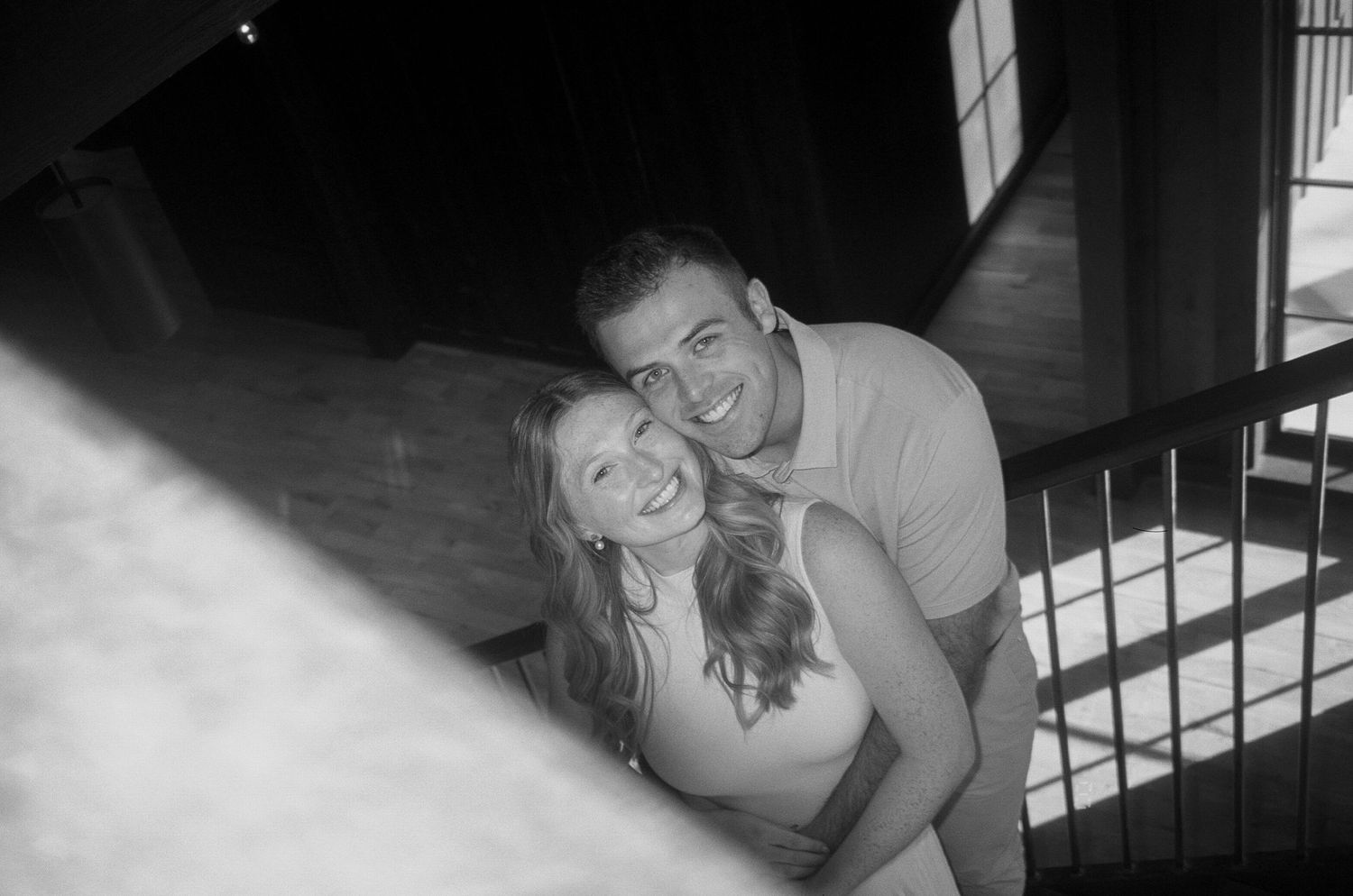 A black and white candid photo of a couple laughing together on stairs in an intimate moment.