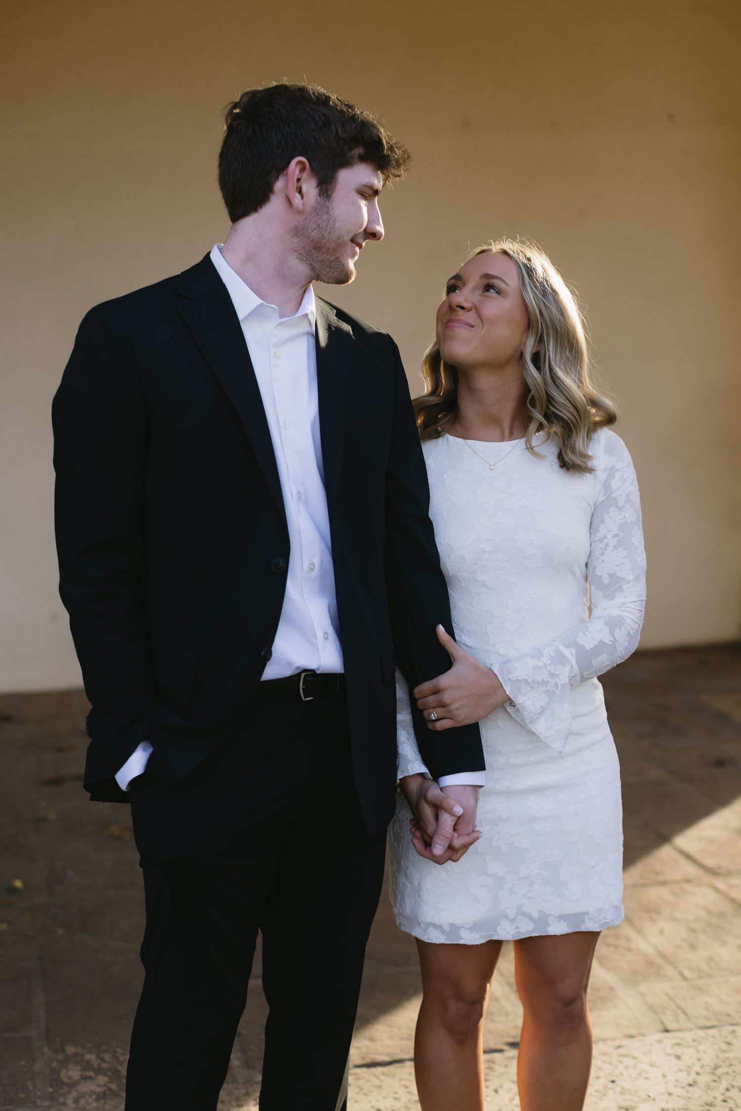 A couple in formal attire shares an intimate moment against a neutral background.