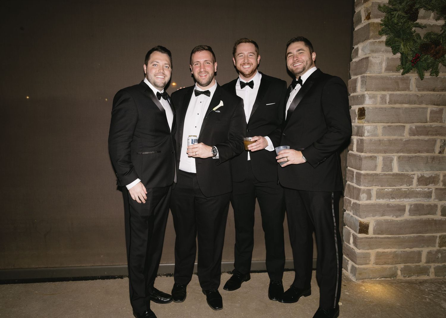 Group of groomsmen in black tuxedos posing together at wedding venue.