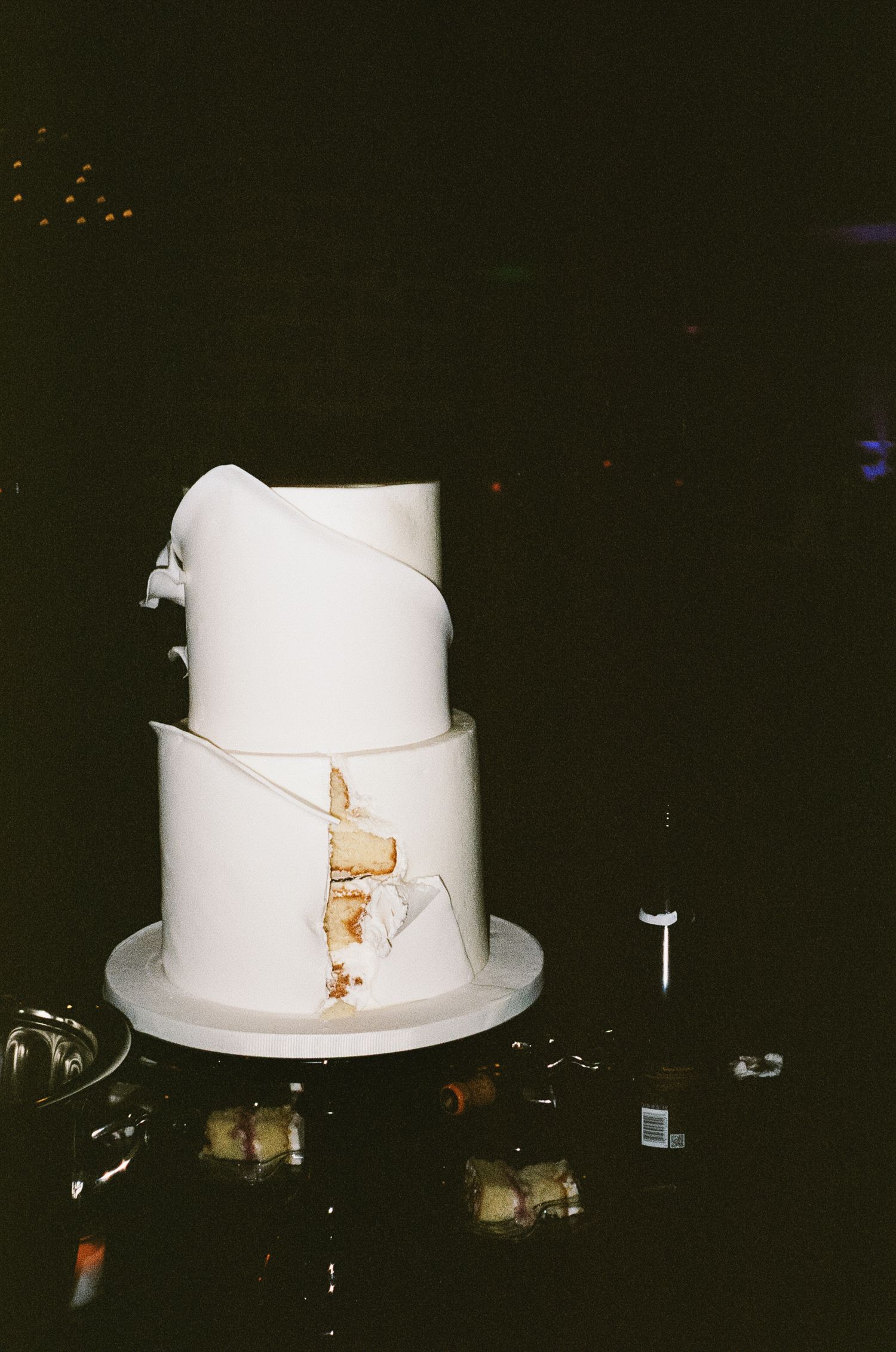 Minimalist white two-tier wedding cake with gold accent detail on dark background.