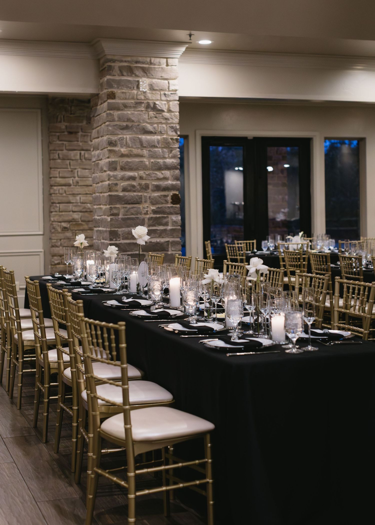 Wedding reception room with stone walls and gold chairs arranged around black-clothed tables.