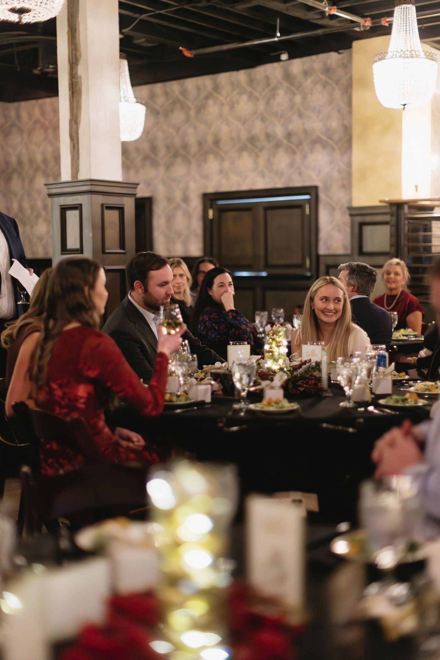 Diners seated at tables in a restaurant with white pendant lights and festive holiday decor.
