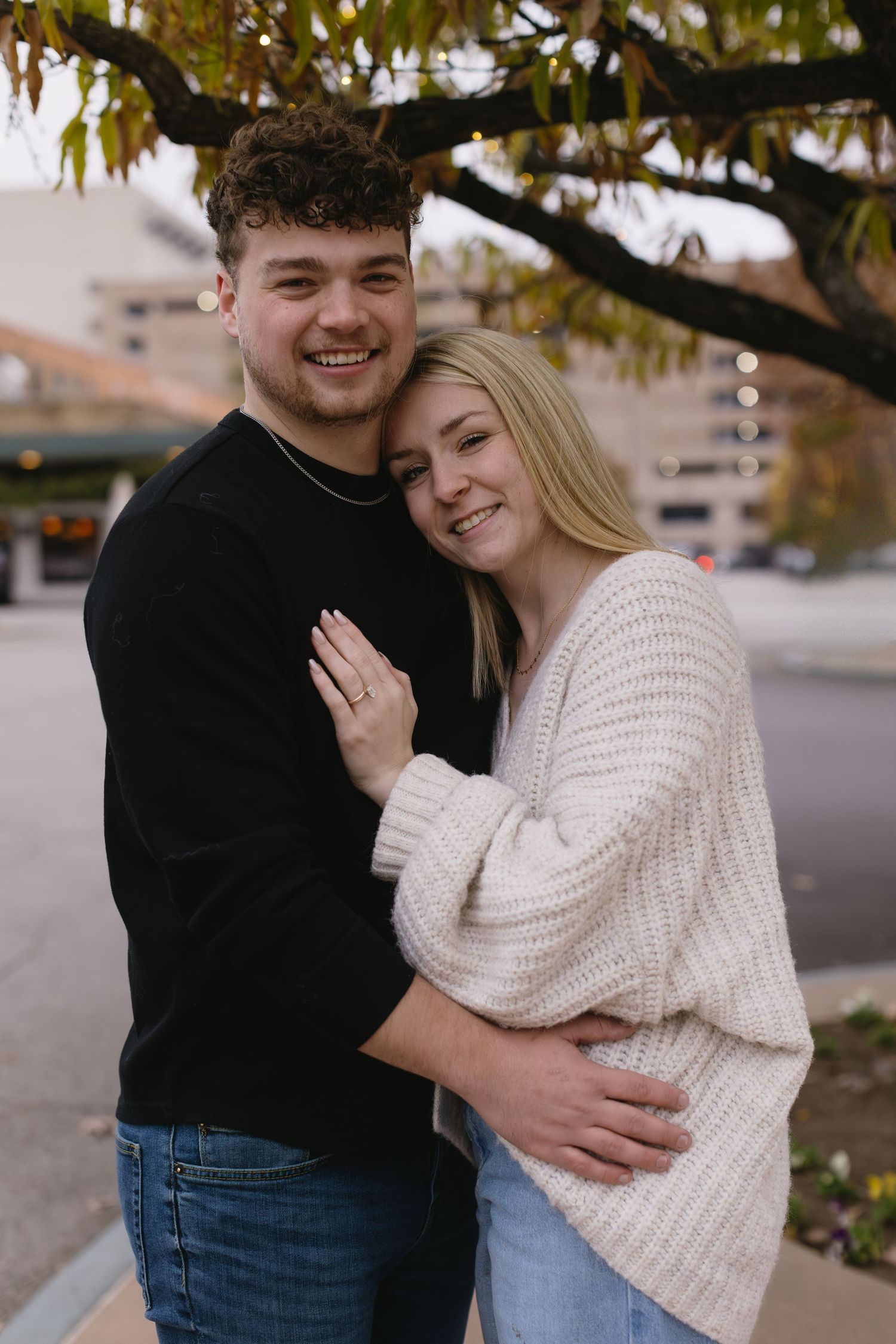 A couple in casual autumn outfits embrace and laugh together outdoors.