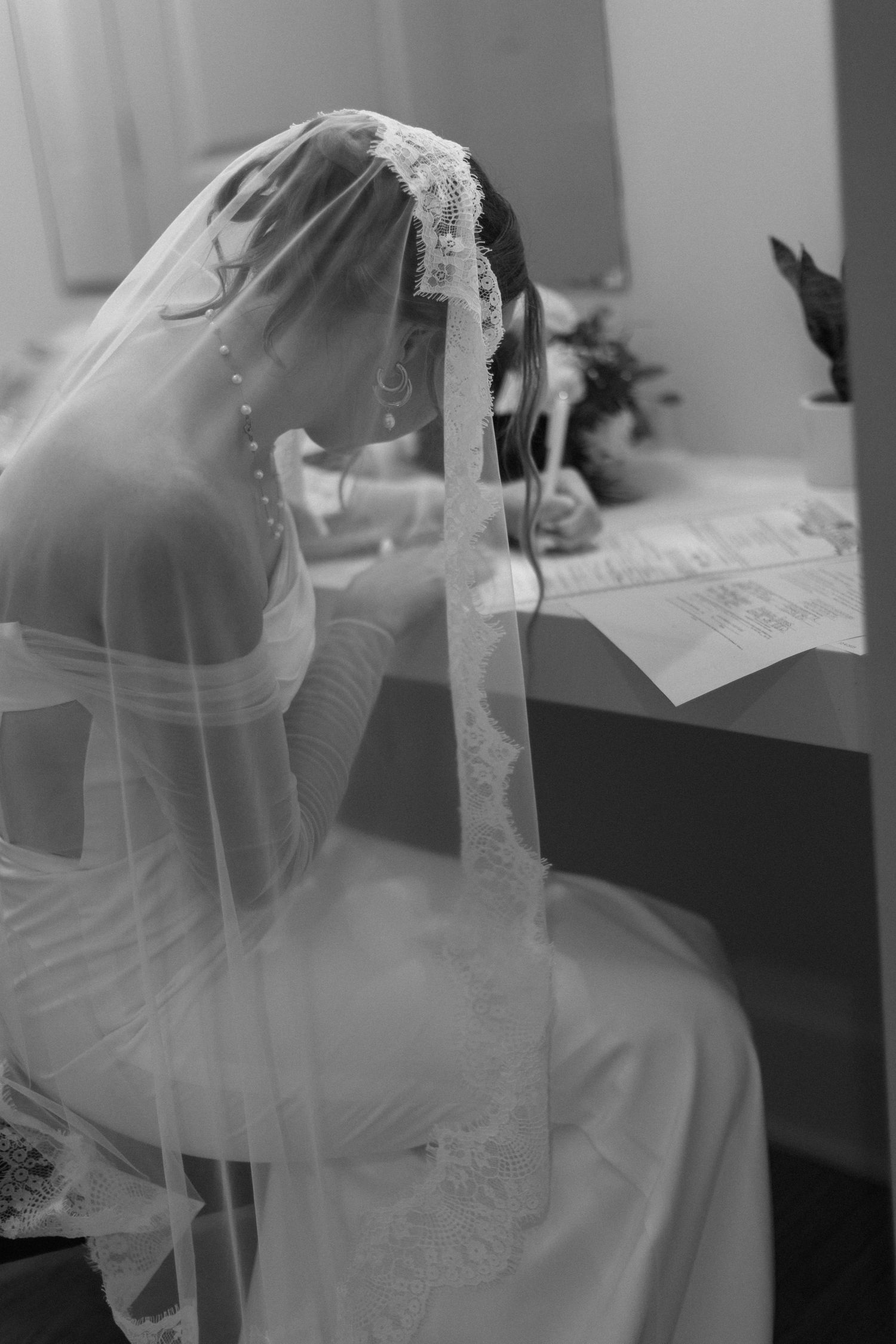 A sequence of black and white photos showing a bride in a veil signing documents at a table.