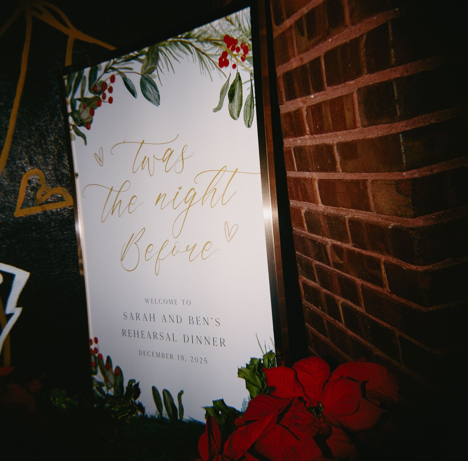 Wedding signage with floral decorations against a brick wall.
