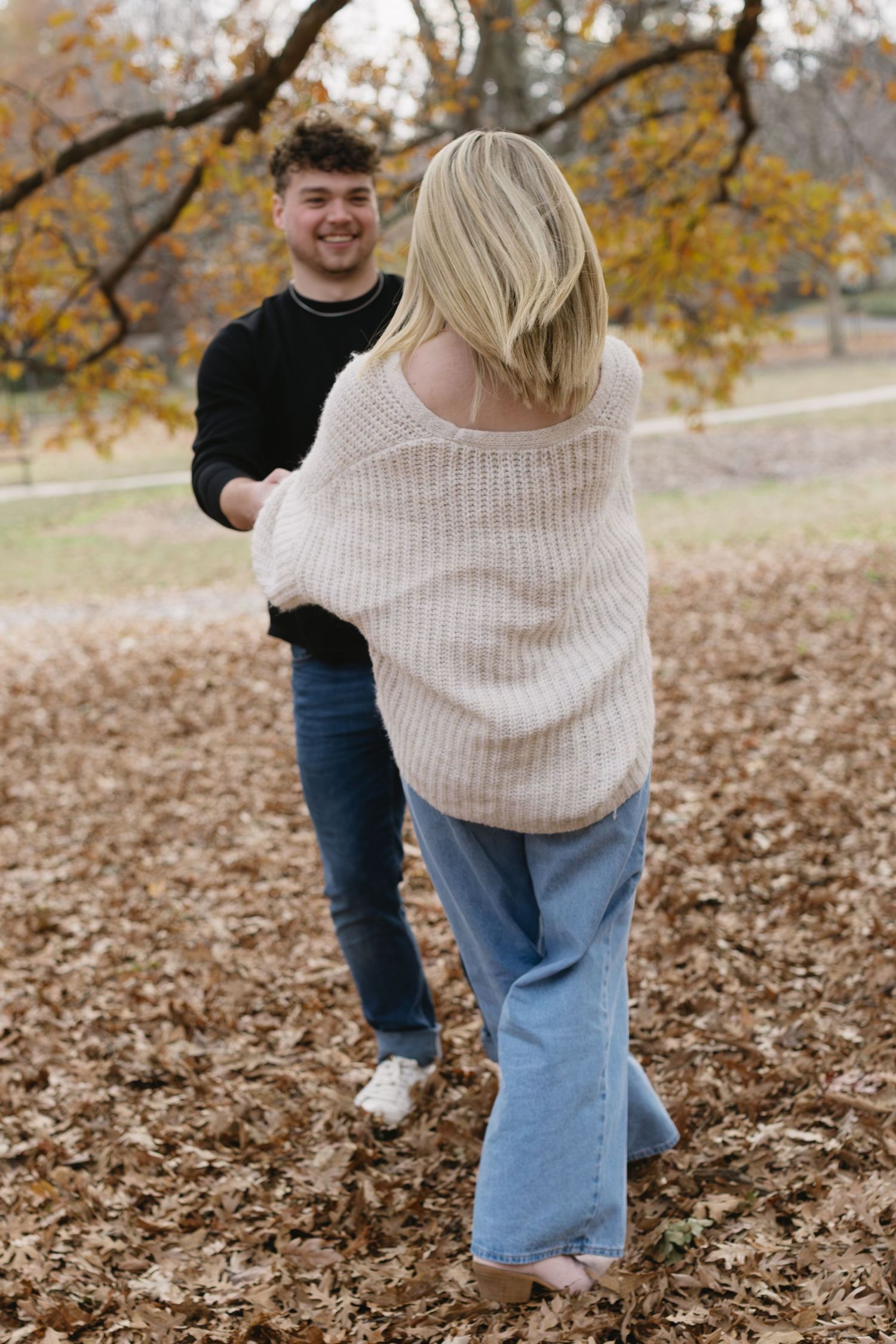 Playful autumn photoshoot with fallen leaves and casual outfits in a park setting.