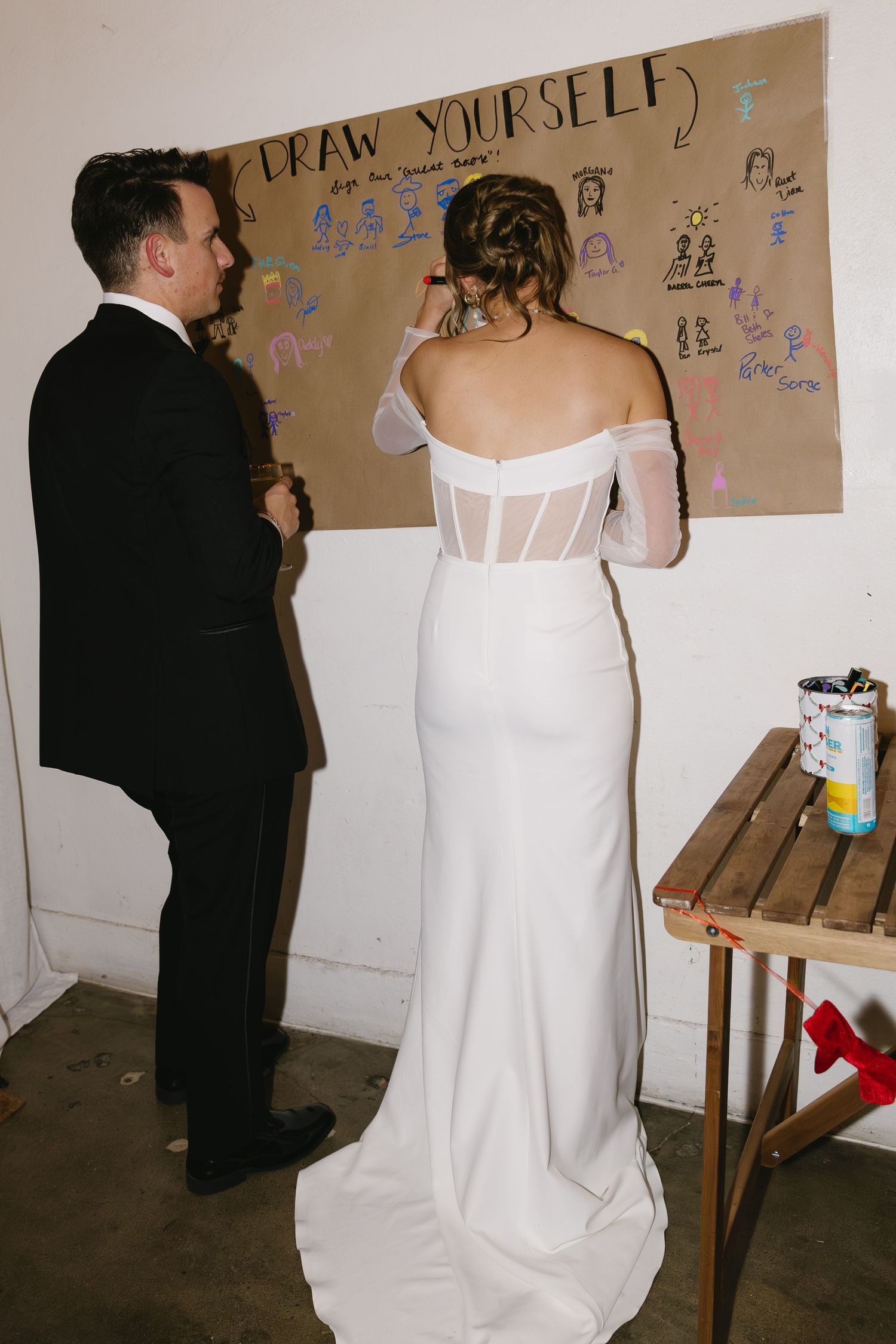 A paper banner on a wall with people drawing or writing on it at what appears to be an event.