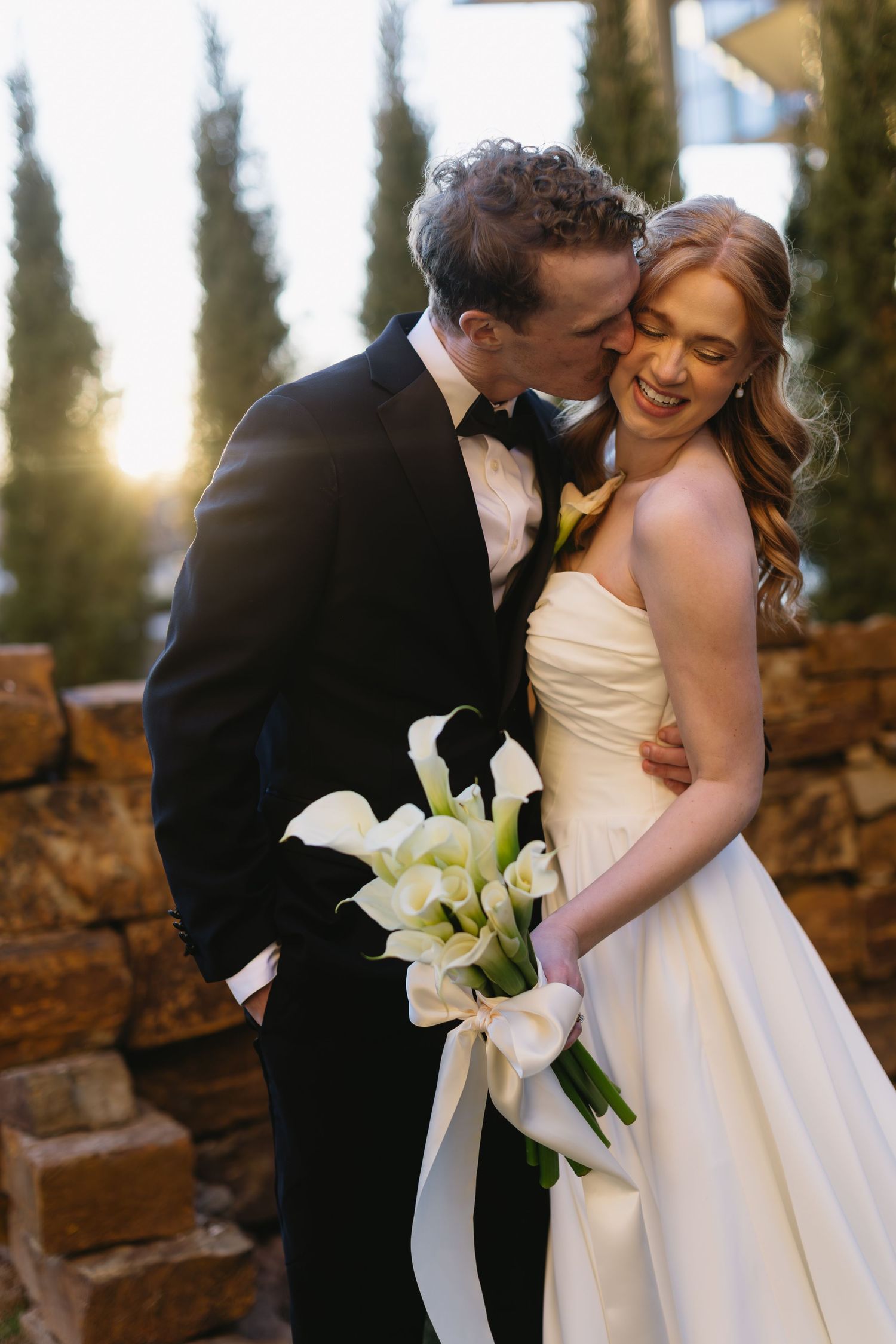 Romantic wedding photos at sunset with white calla lily bouquet among cypress trees.