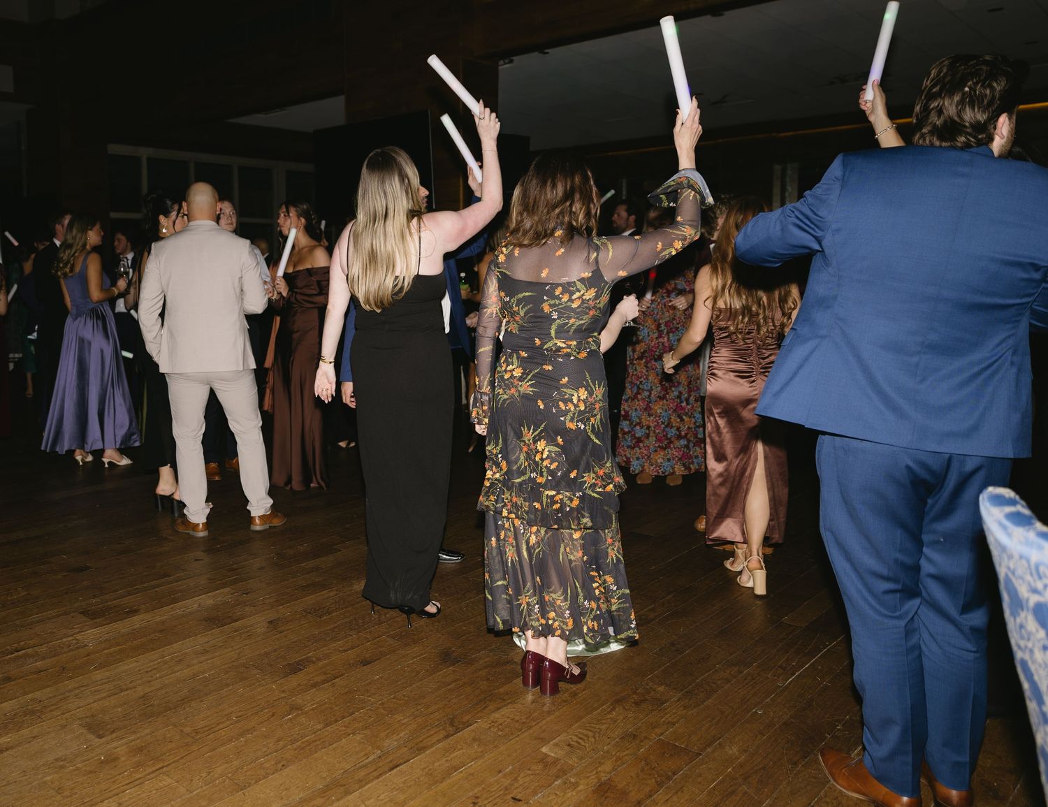 Wedding guests dancing and celebrating on a dimly lit dance floor.