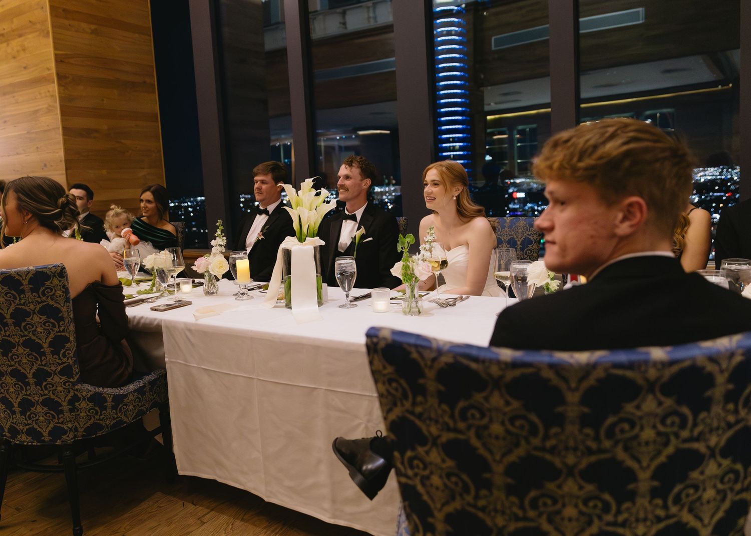 A formal dining setup with white tablecloths and patterned chairs in a dimly lit reception room.