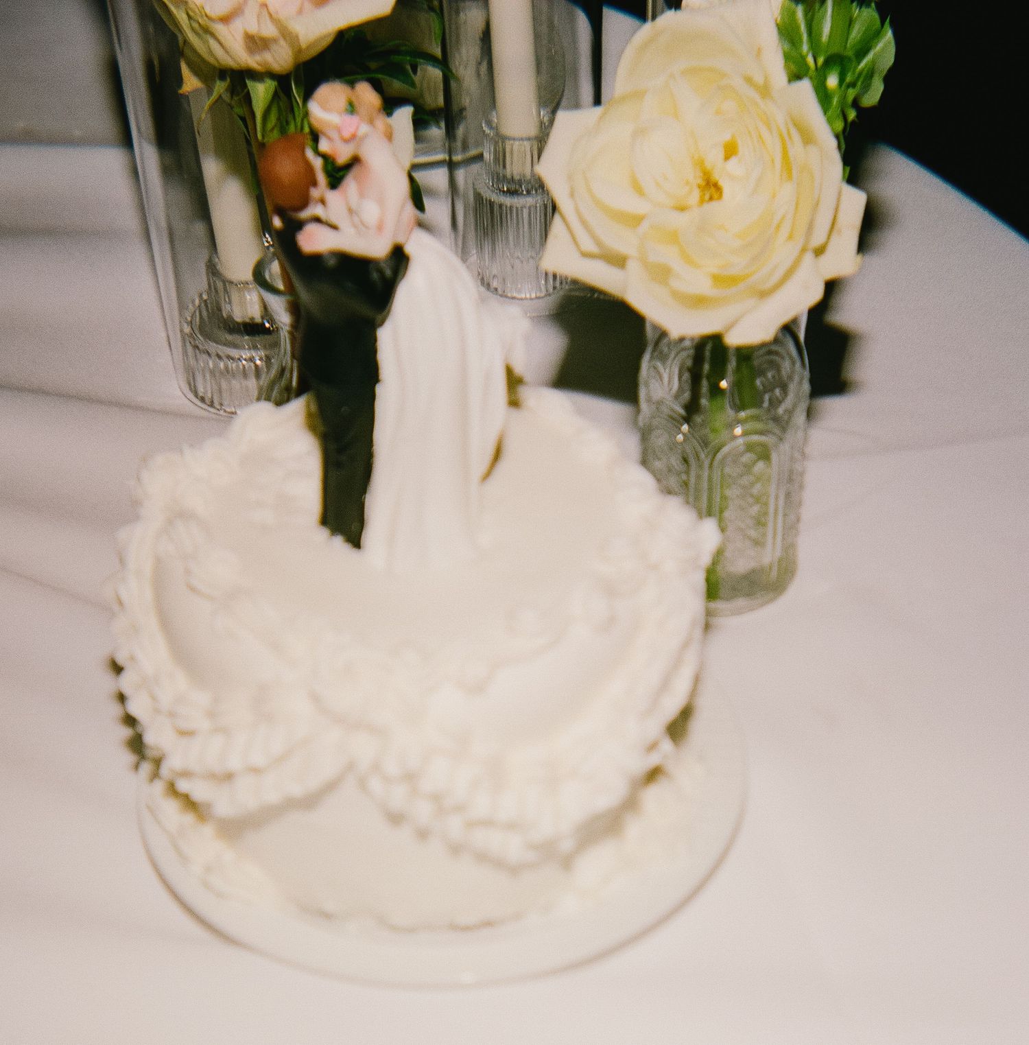 Delicate cream roses and glassware arrangements on white tablecloth at wedding reception.