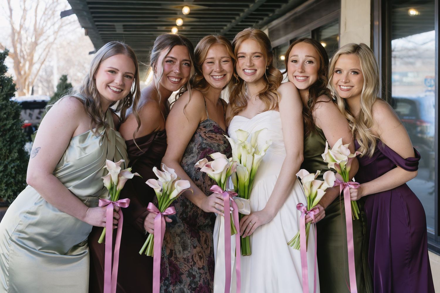 Bridesmaids in purple dresses hold bouquets while posing together at a wedding celebration.