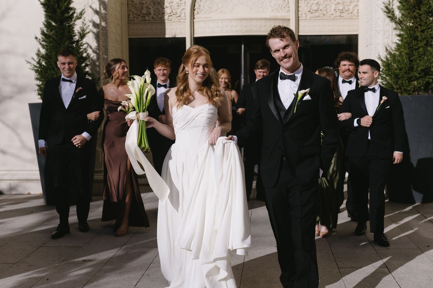 Wedding party walking outside a grand building with classical architecture.