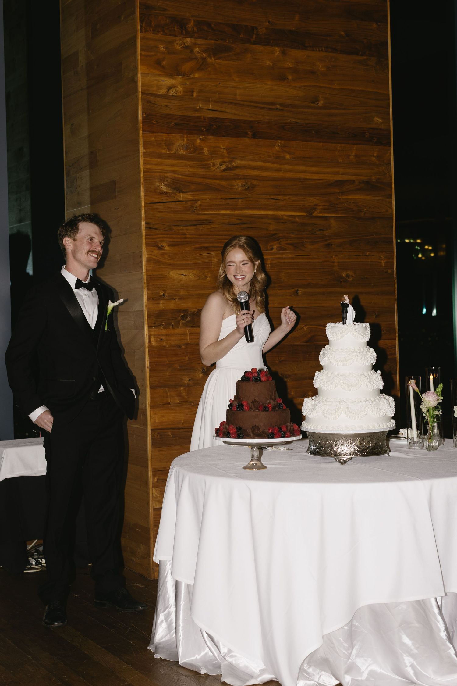 Wedding reception setup with multiple white-clothed tables displaying elegant cakes and desserts.