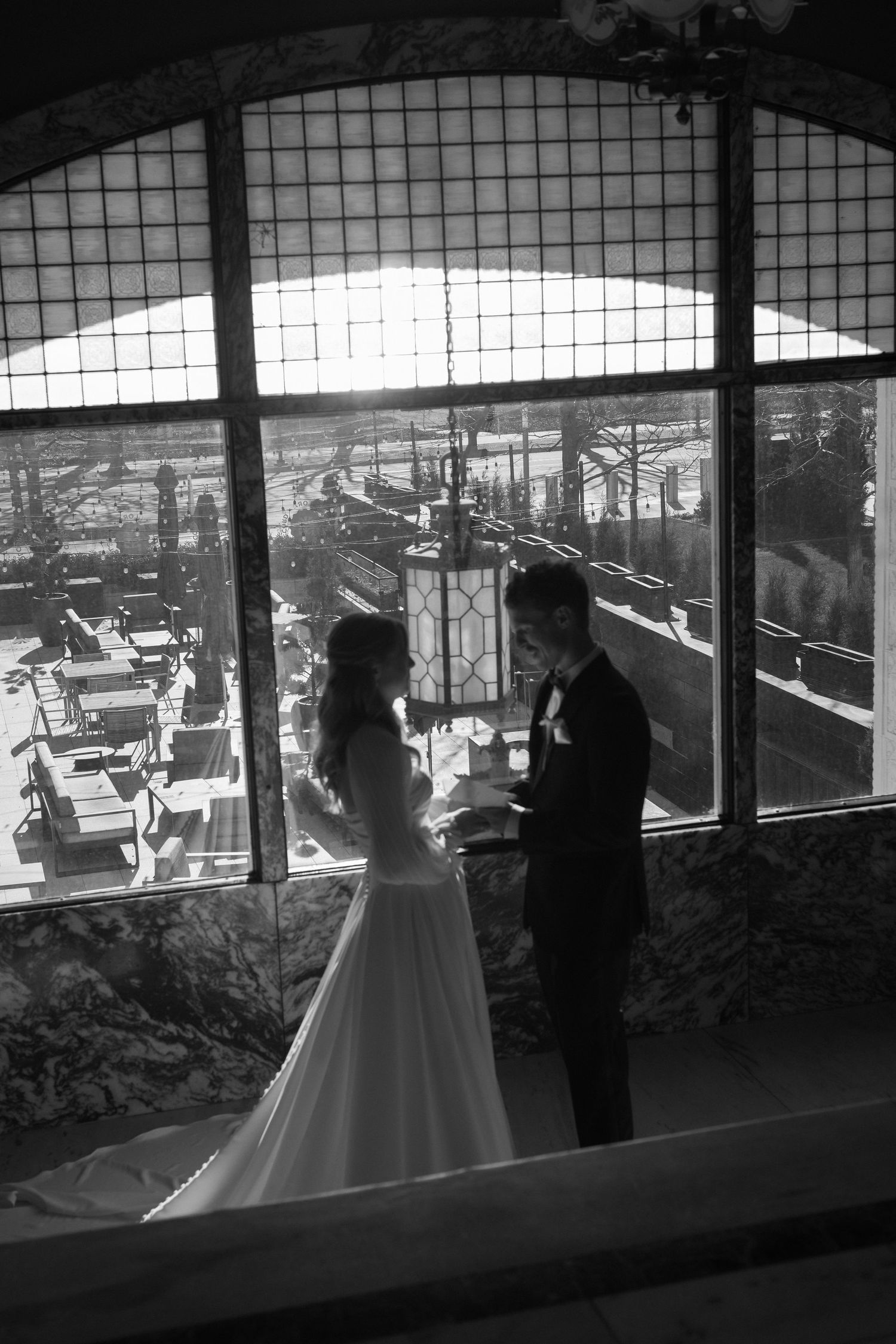 A wedding couple silhouetted against large windows in a rustic venue, shown in a series of black and white frames.