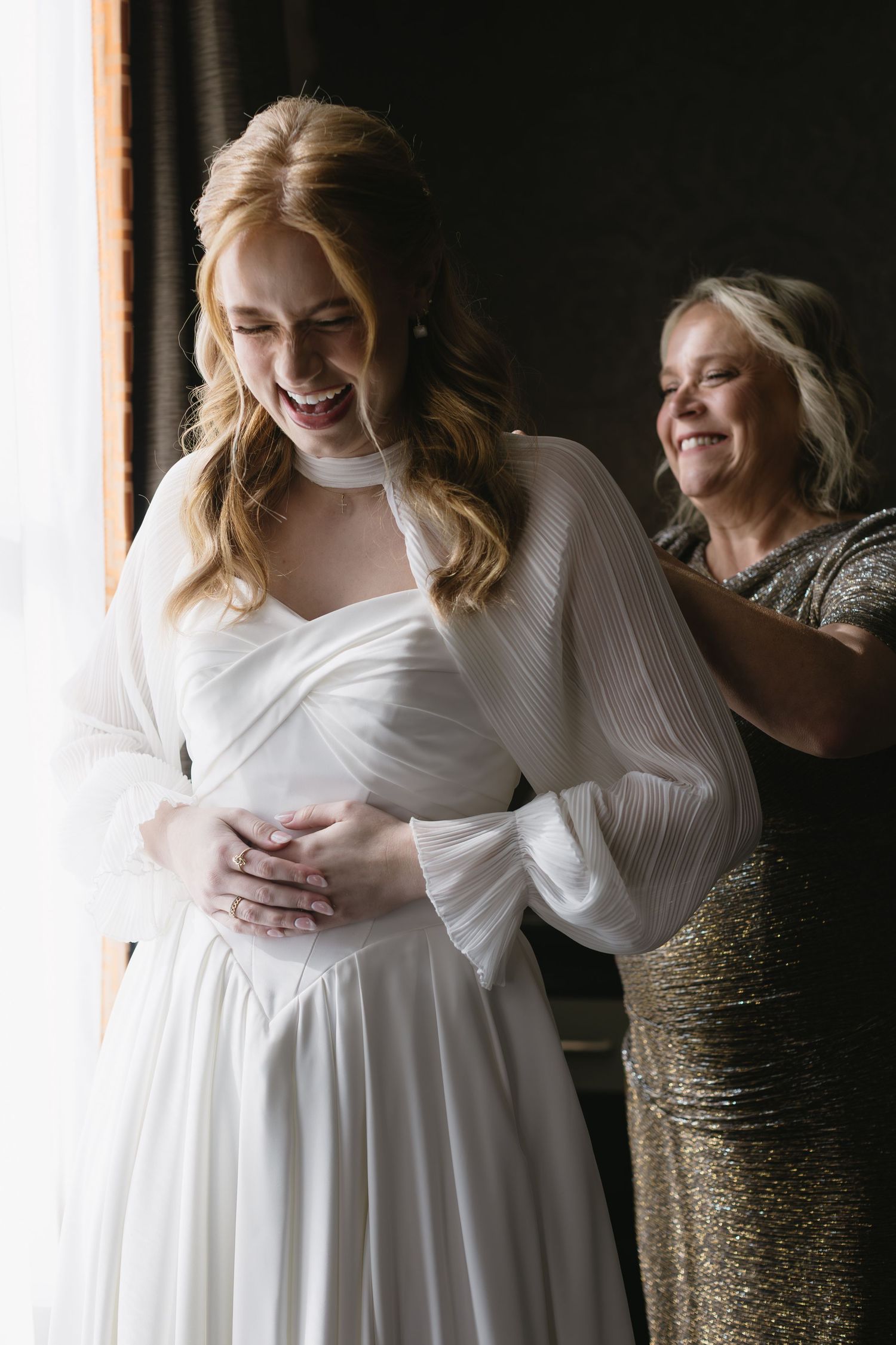 Emotional moments captured during wedding dress fitting with supportive companion in natural light.
