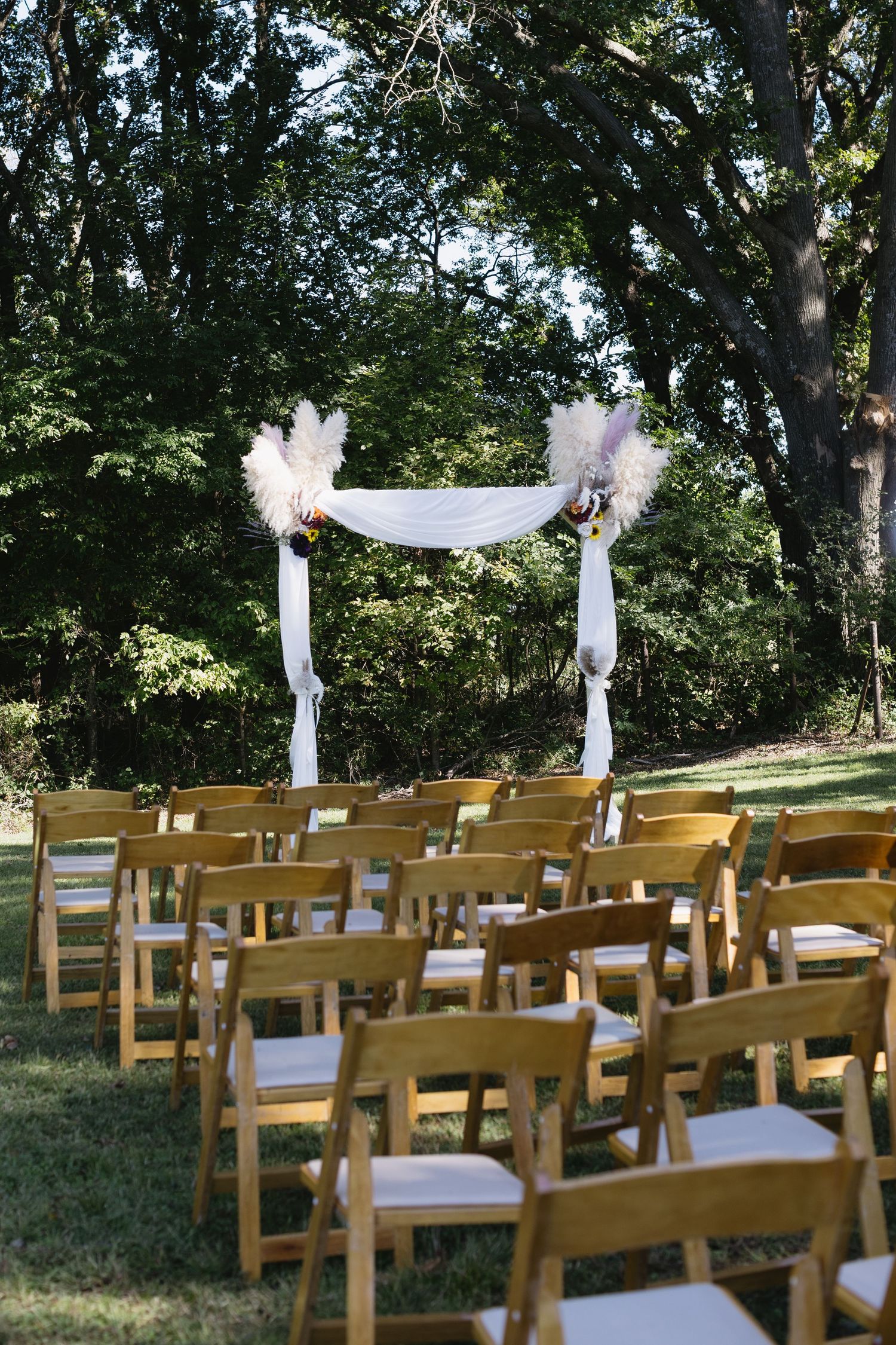 Outdoor wedding ceremony setup with wooden chairs and white fabric decorations.