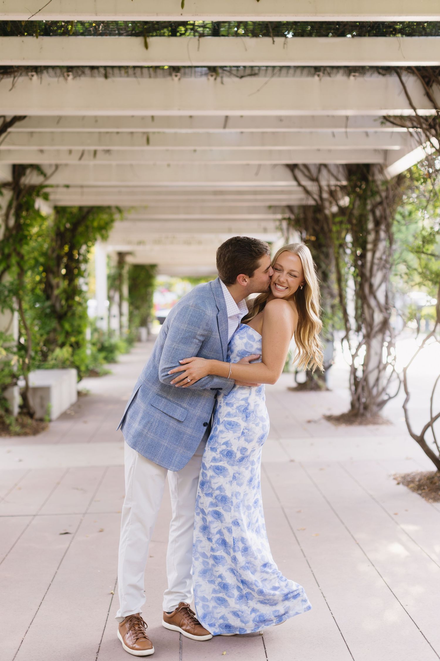 Playful couple sharing intimate moments under a covered walkway with climbing vines.