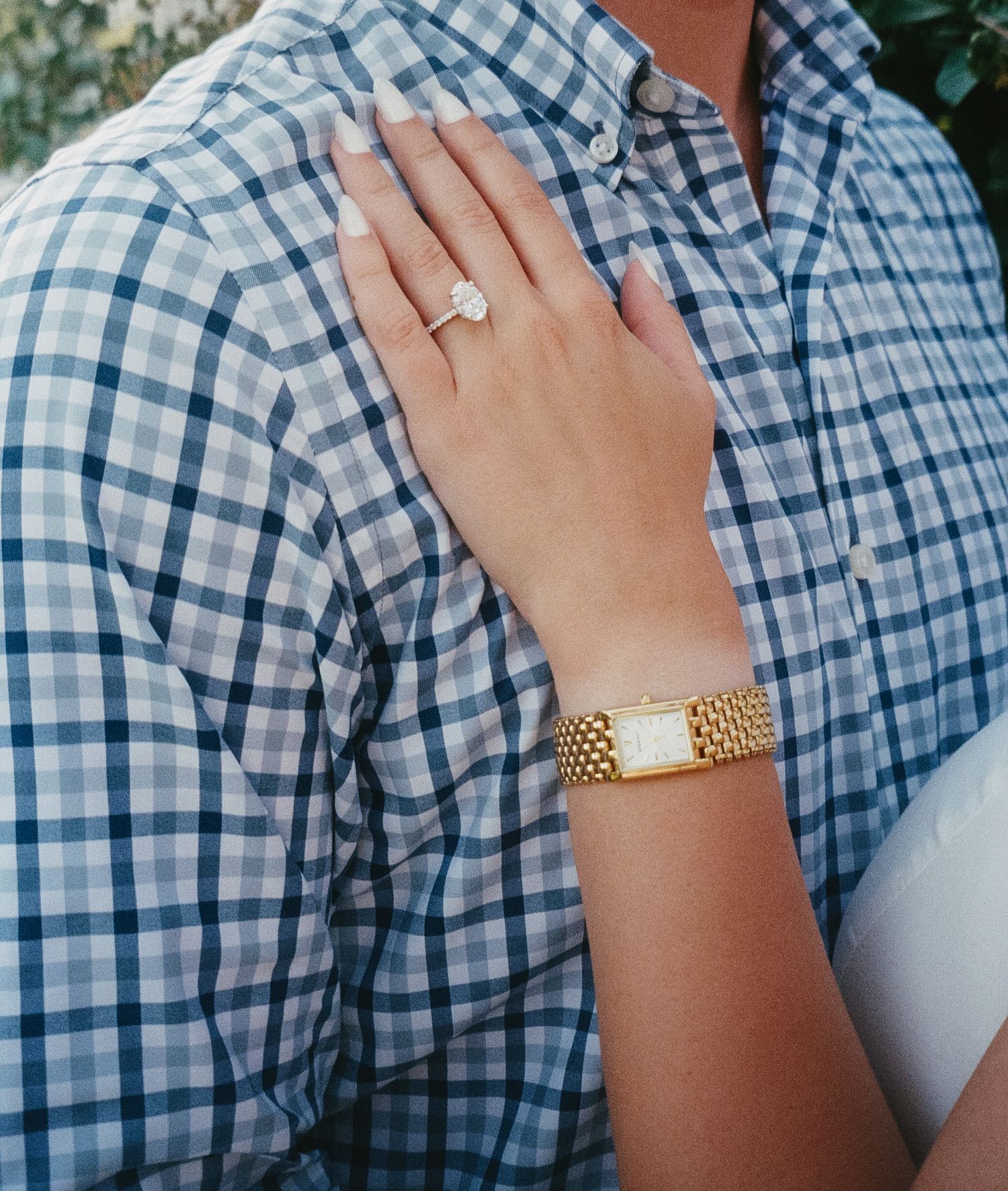 Close-up view of hands wearing a gold watch against a blue and white checkered shirt.