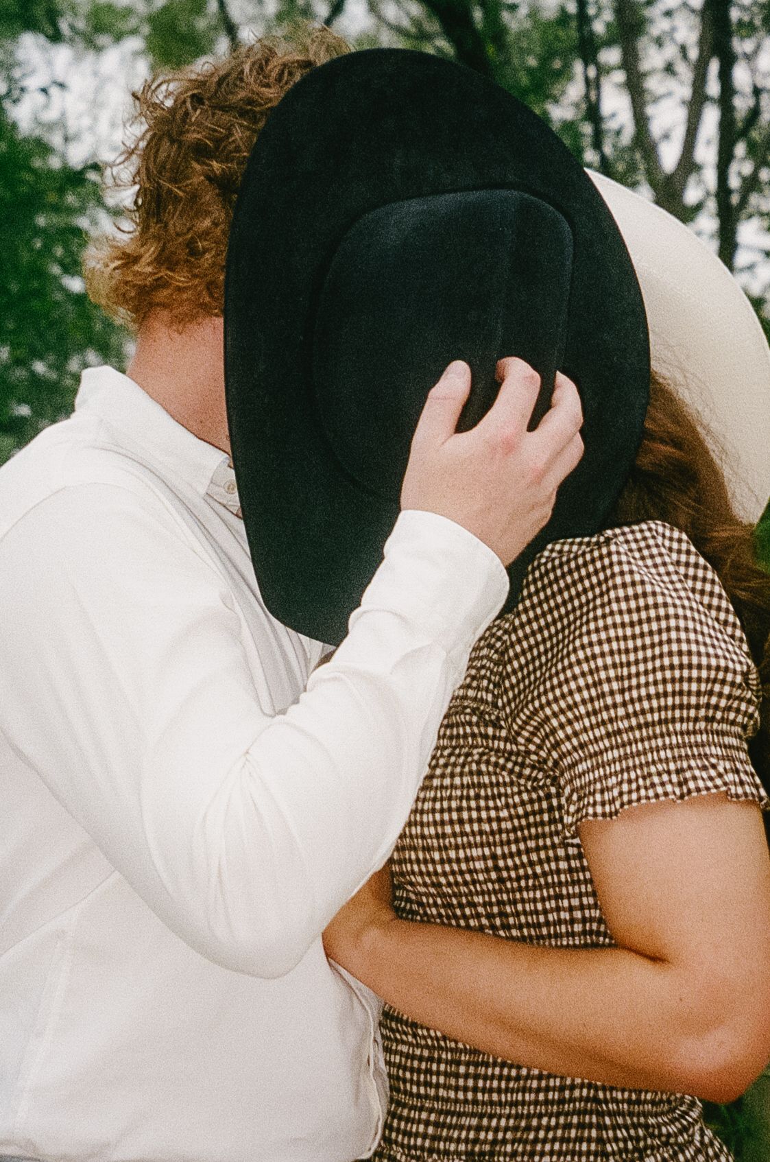 A couple embraces outdoors with one person wearing a white shirt and another in a brown checkered top.