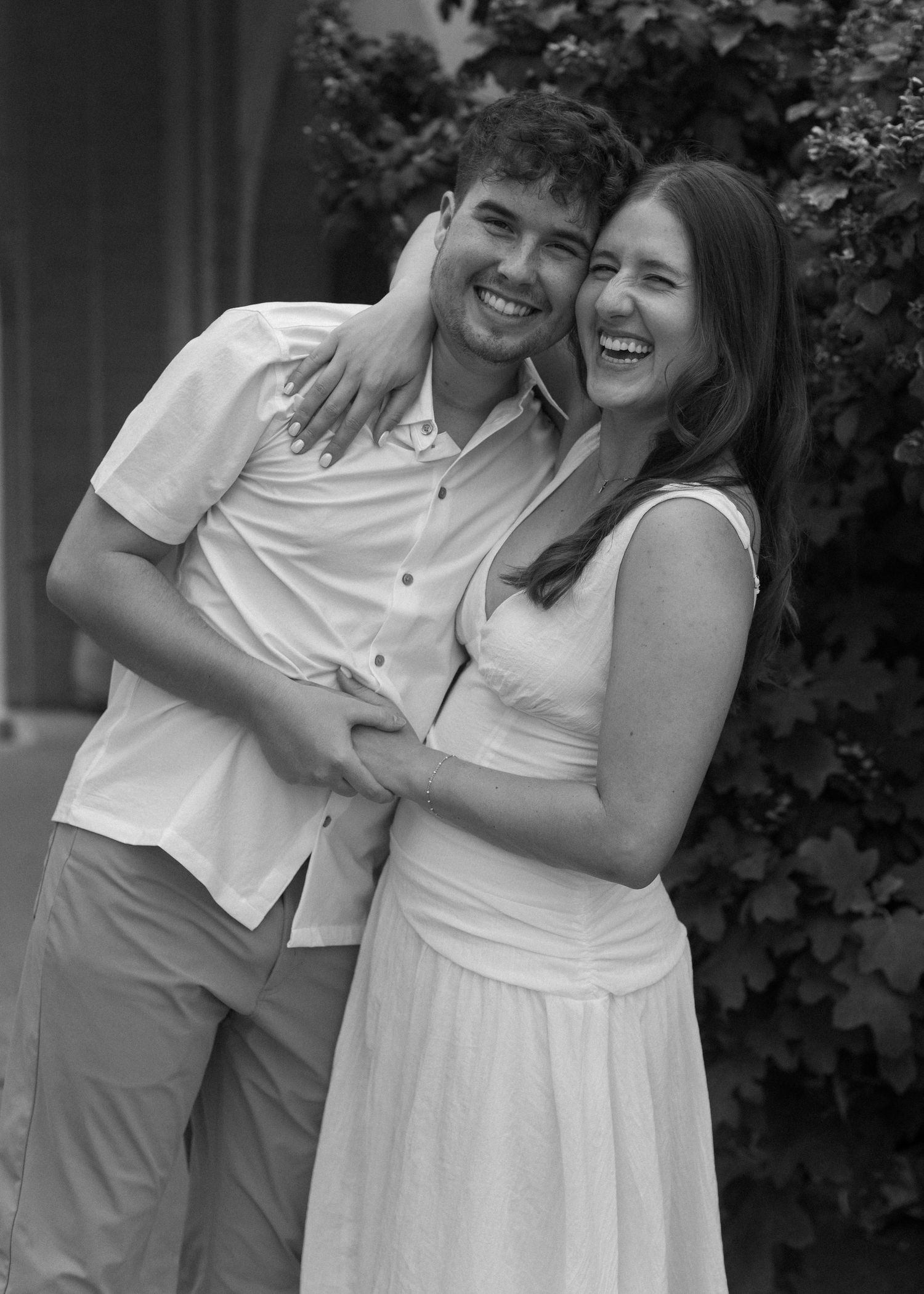 A joyful black and white portrait of a couple laughing and embracing outdoors.