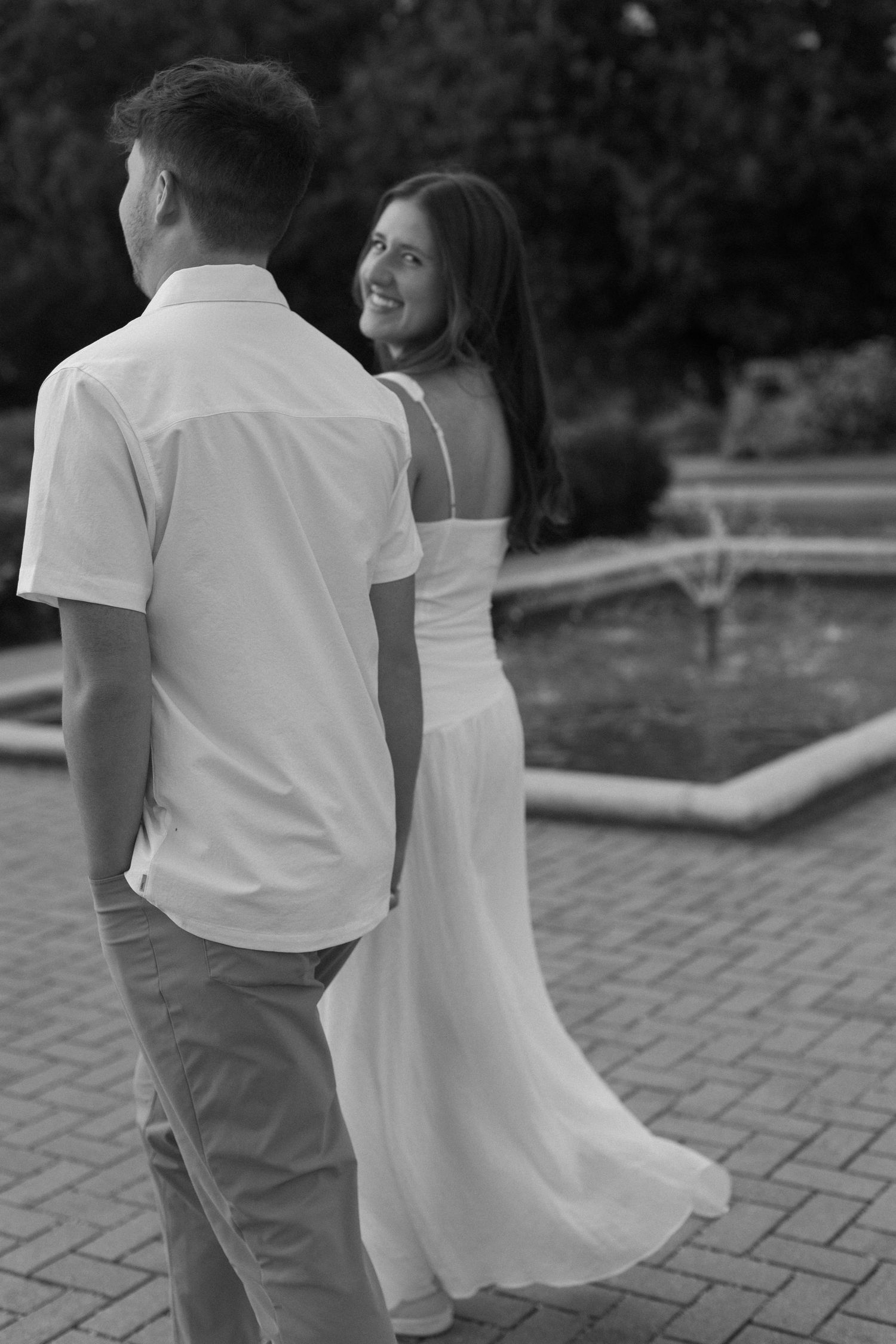 A black and white photo of a couple in white clothing dancing on a brick patio.