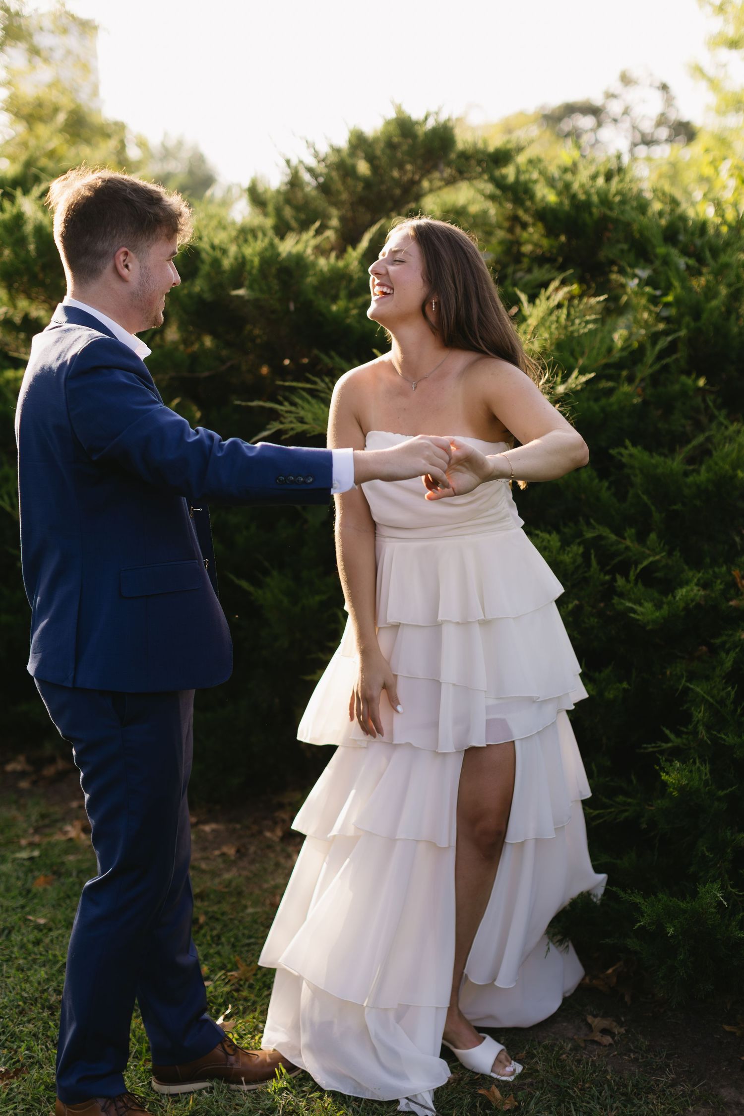 A couple in wedding attire share a joyful dance moment outdoors.