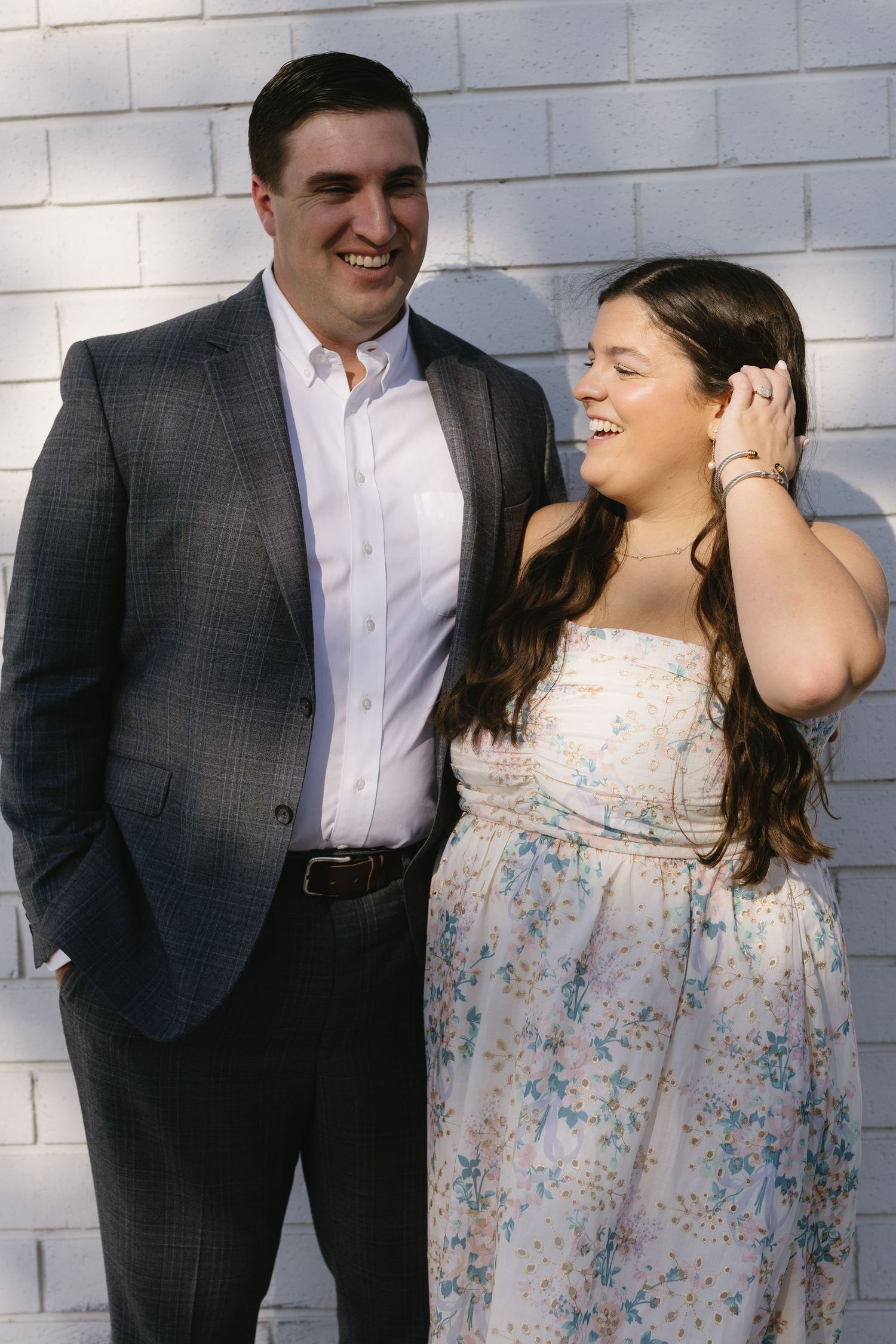 Playful couple laughing and posing against a white brick wall.