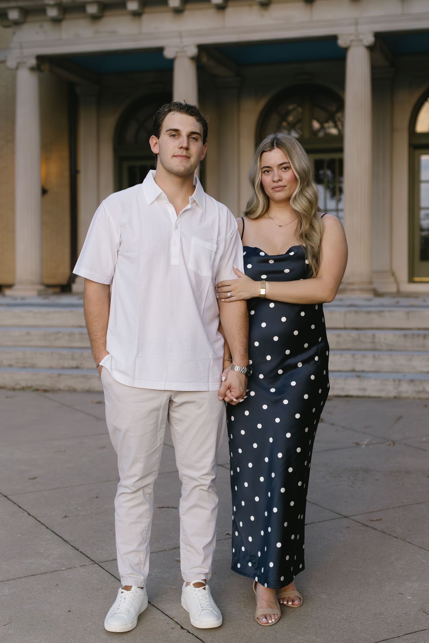 Couple poses together on stone steps, with her in polka dots and him in all white.