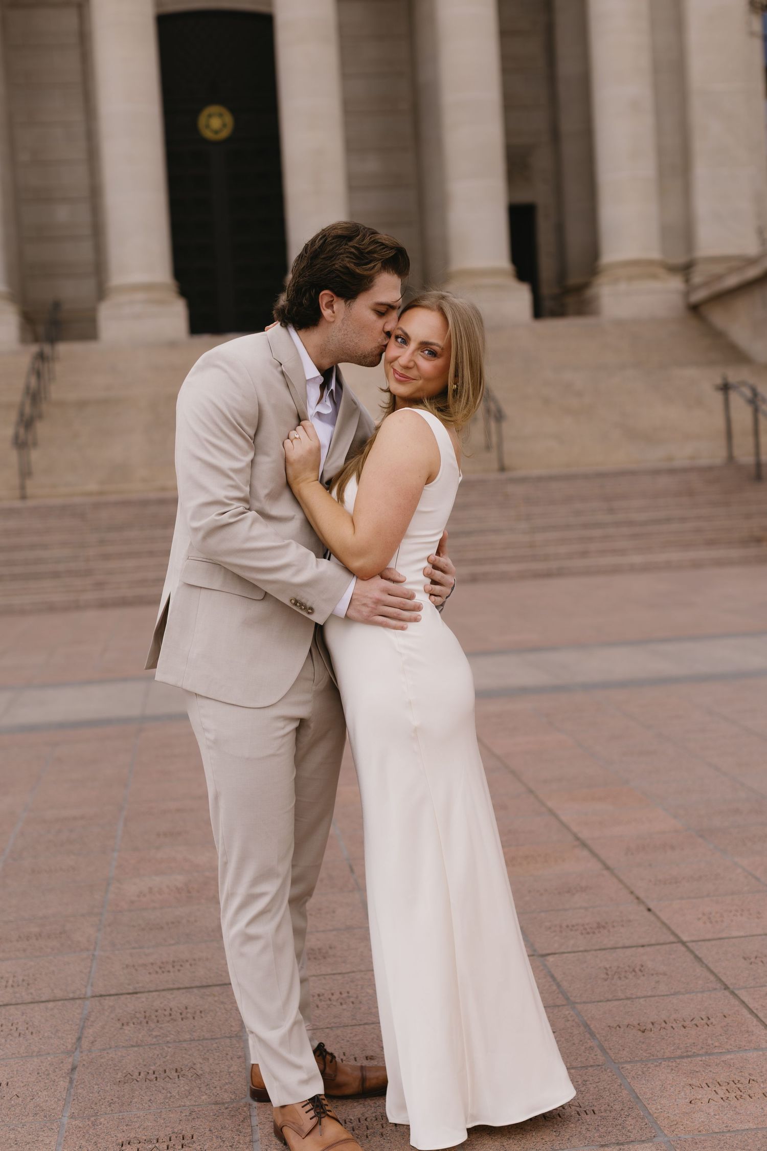 A romantic moment between a couple in coordinated formal wear outside a classical building with columns.